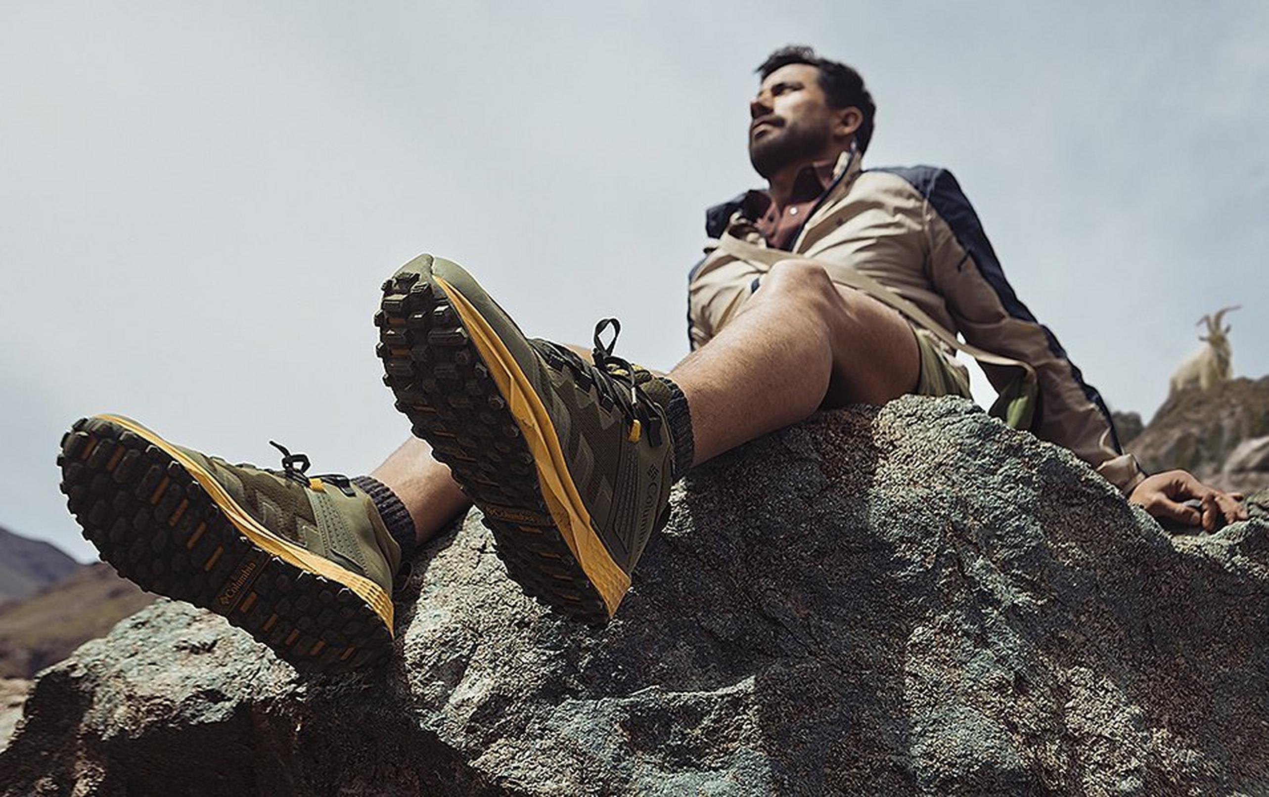 A hiker sits on a rock dangling his Columbia Sportswear Facet 75 Mid shoes over the edge.