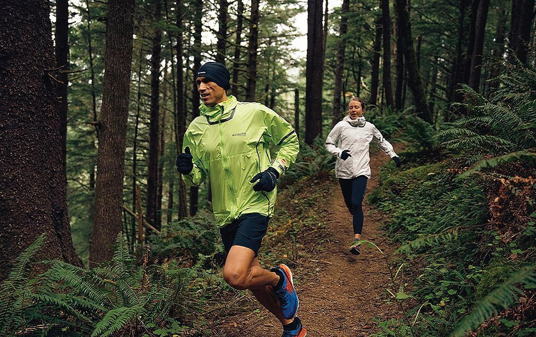 Man and a woman running on a forest trail.