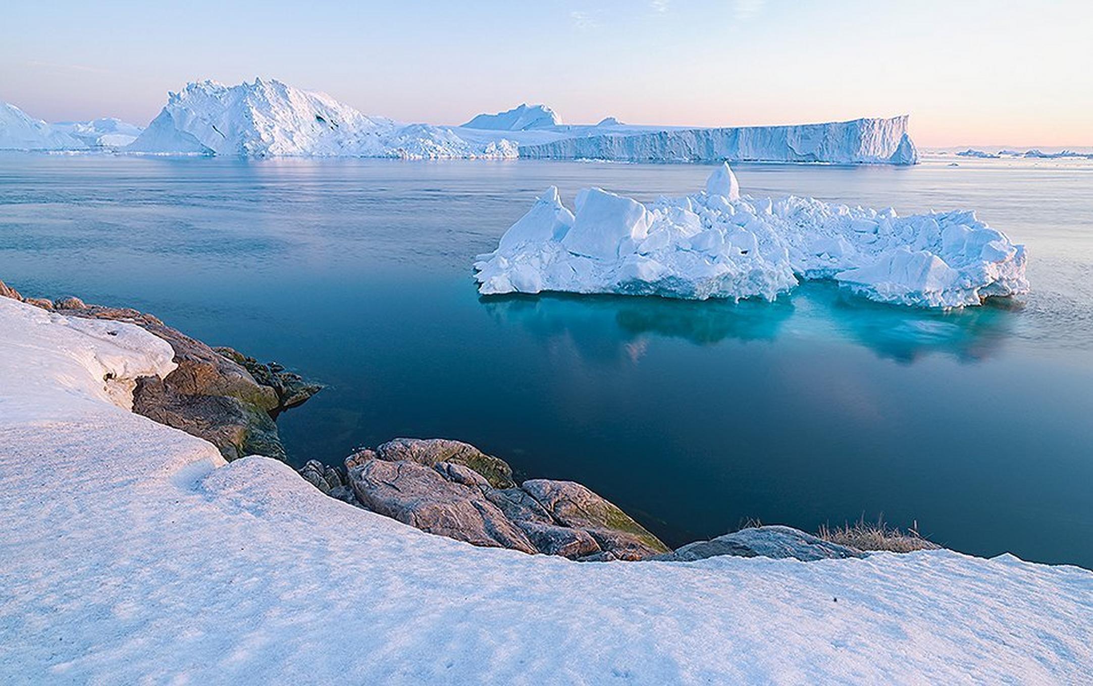 A stunning photo depicting beautiful snow white ice caps in Antarctica with aqua-blue water surrounding them.