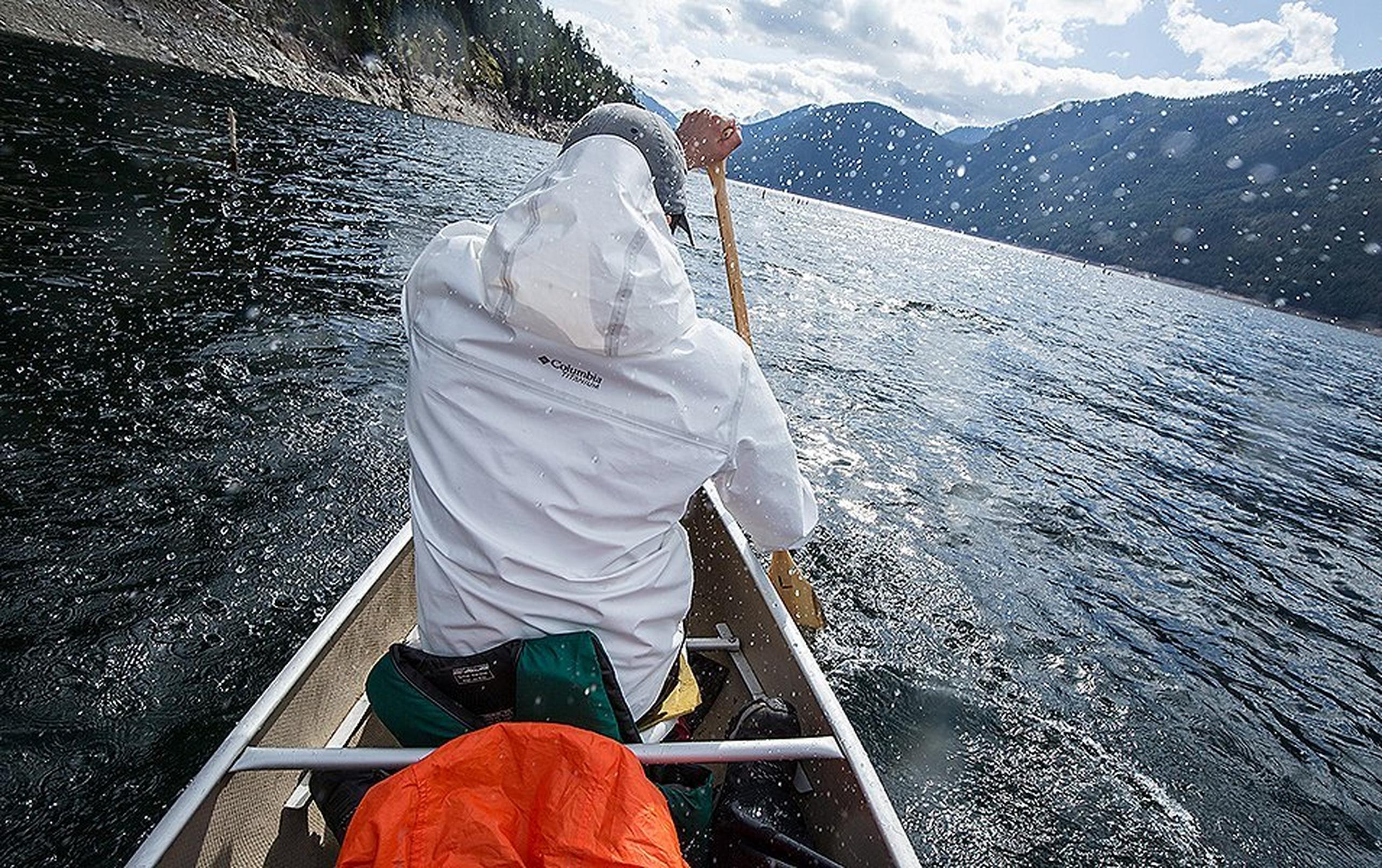 A man wearing a white Columbia Sportswear OutDry™ Extreme jacket paddles away from the camera in a canoe.