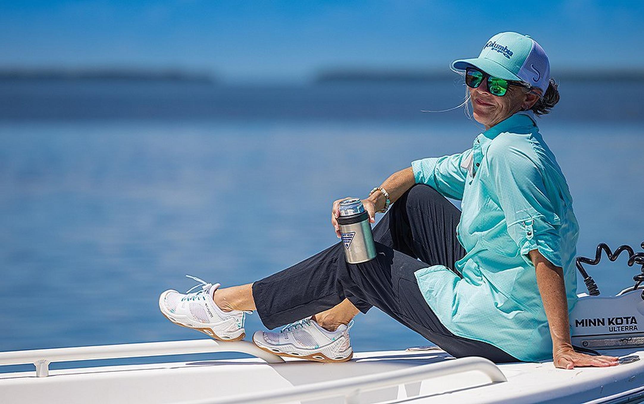 A woman in a UPF fishing shirt sits on a boat on a beautiful sunny day.