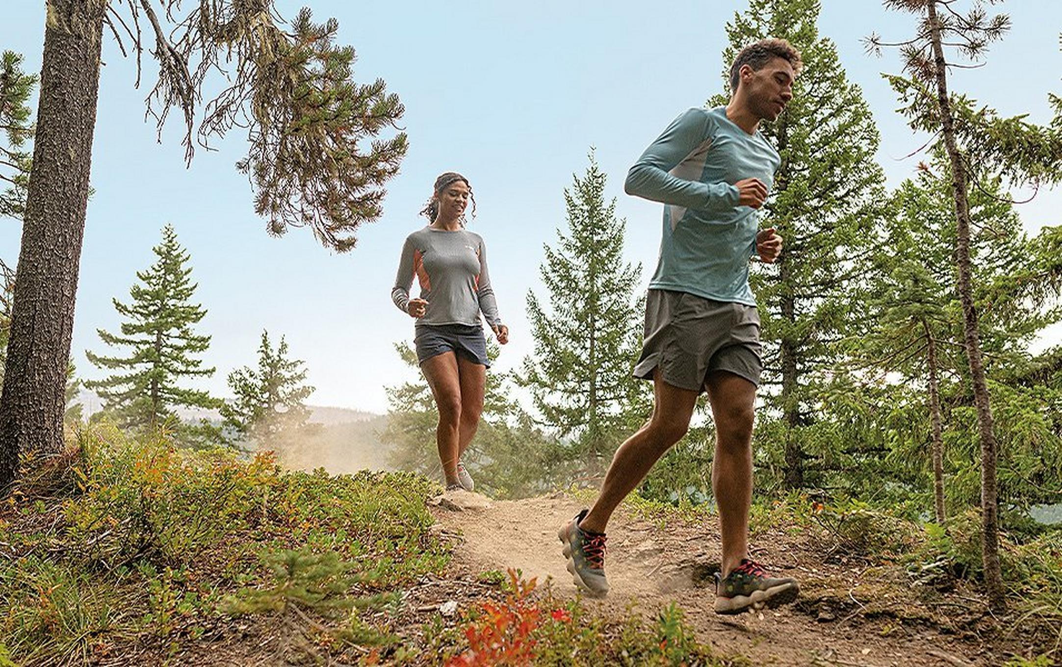 A trail runner wearing UPF-rated clothing runs down a path with a woman jogging behind him.