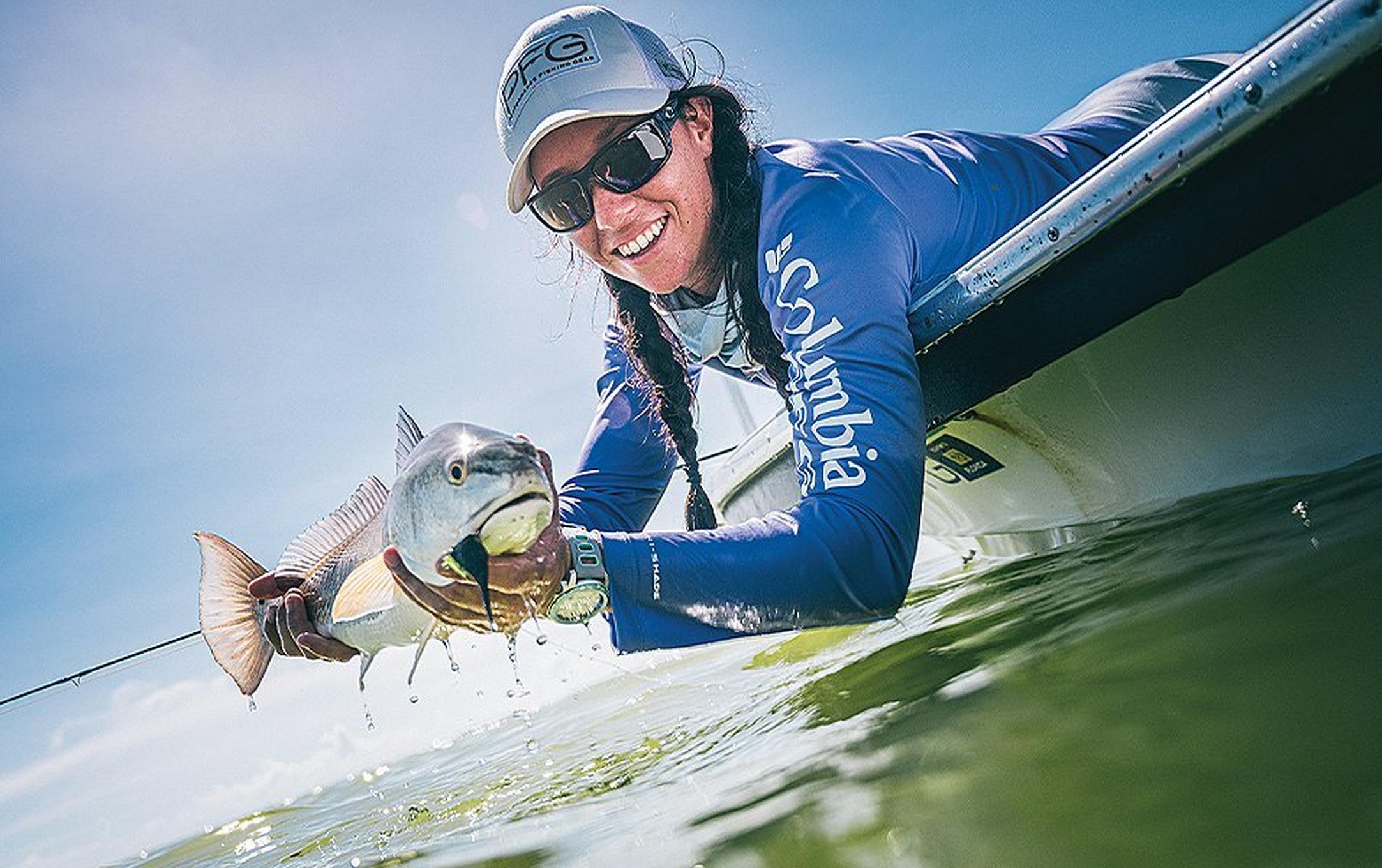 Woman leaning over boat holding a fish.