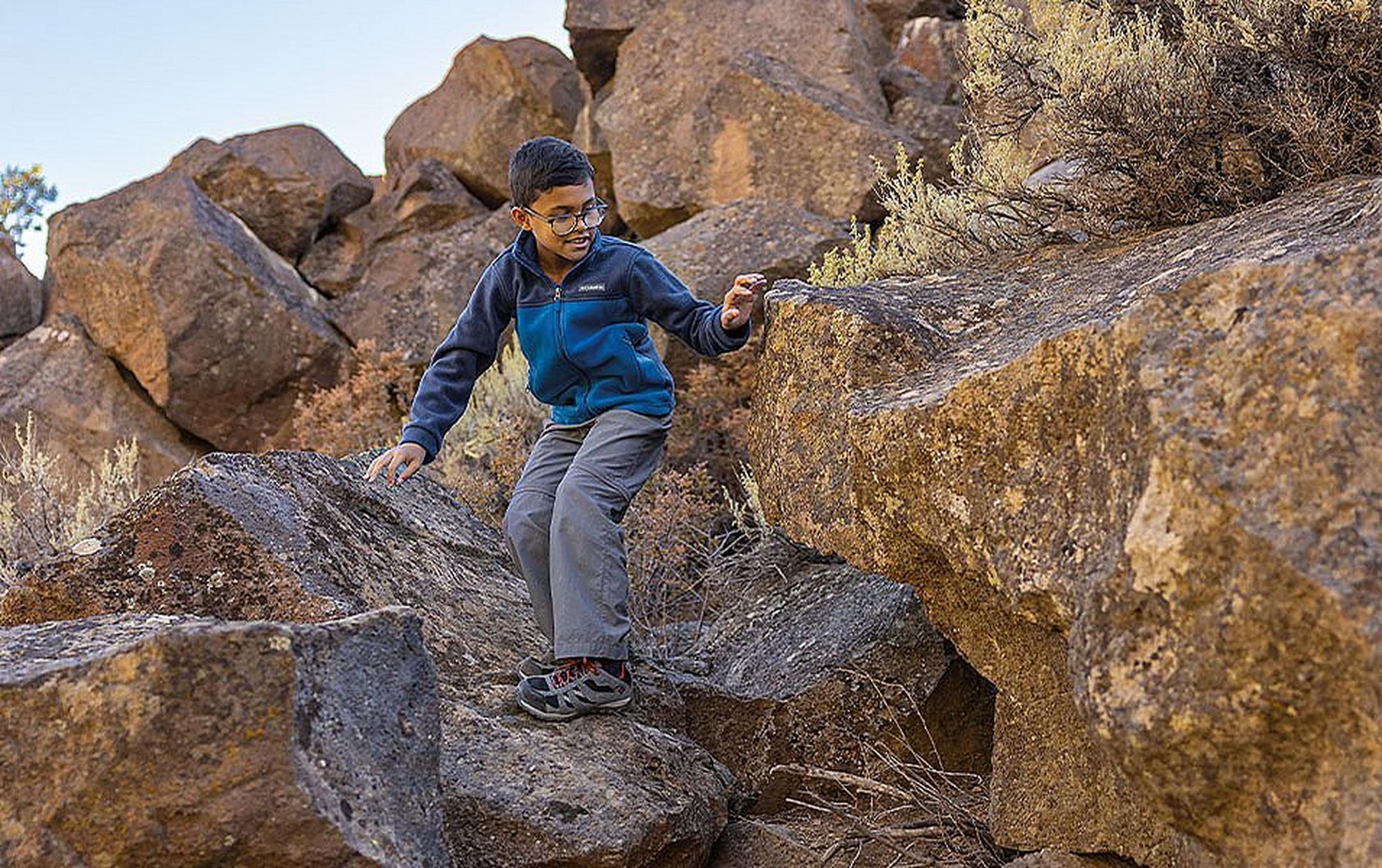 A boy climbs down a hiking trail through large boulders with a smile on his face.