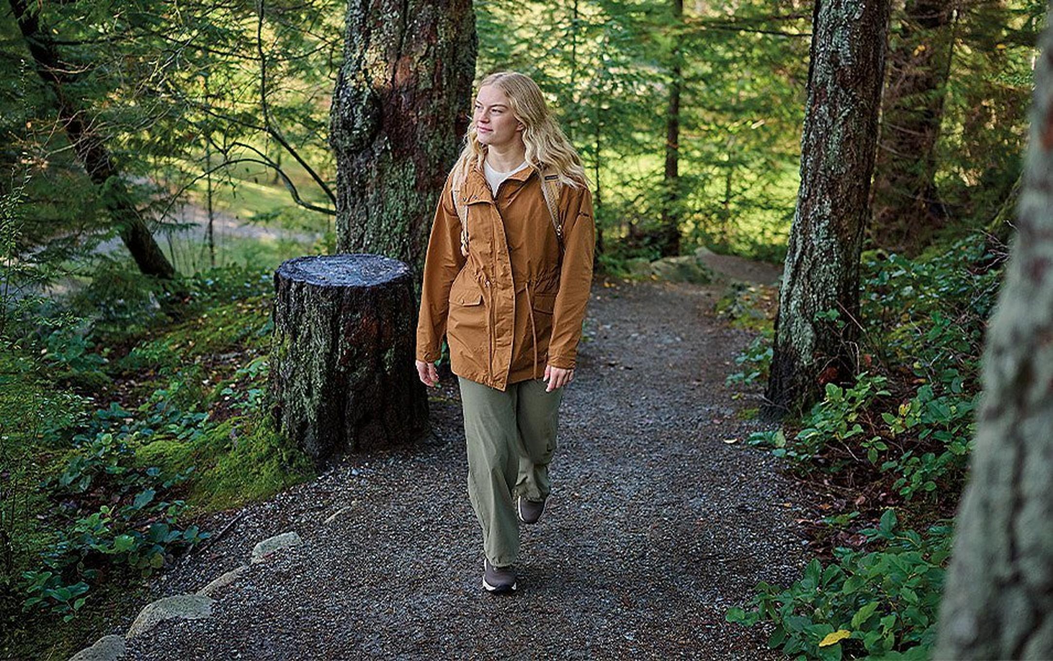 A young woman strolls in solitude through a dense, green forest.