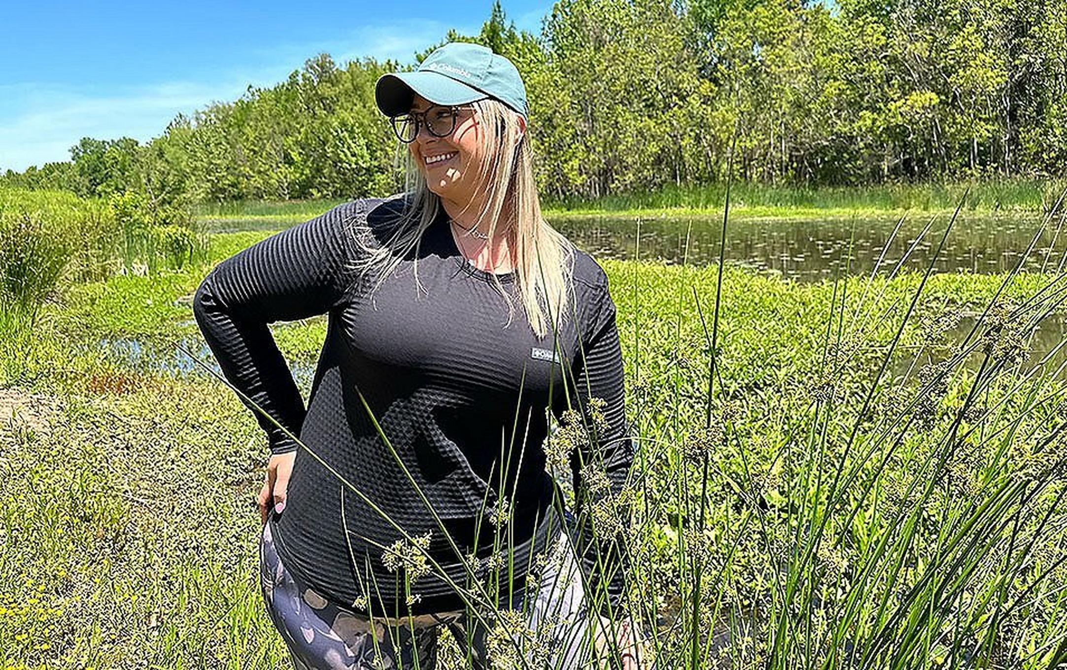 Chelsea McCurdy stands amid green foliage in Allsopp Park, Arkansas, wearing Columbia Sportswear’s Leslie Falls long sleeve hiking top.