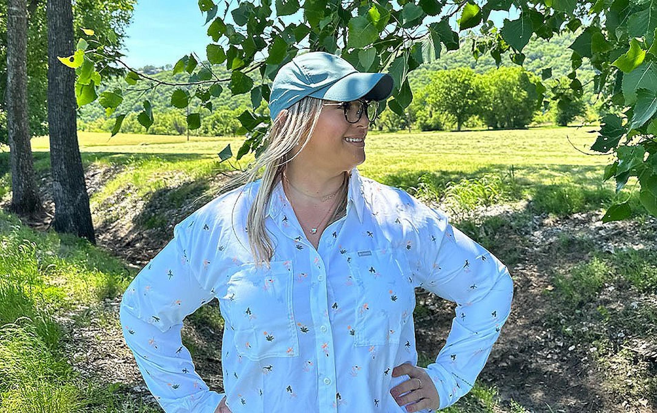 Chelsea McCurdy stands in a sunny field with trees all around her wearing Columbia Sportwear’s Silver Ridge Utility shirt.