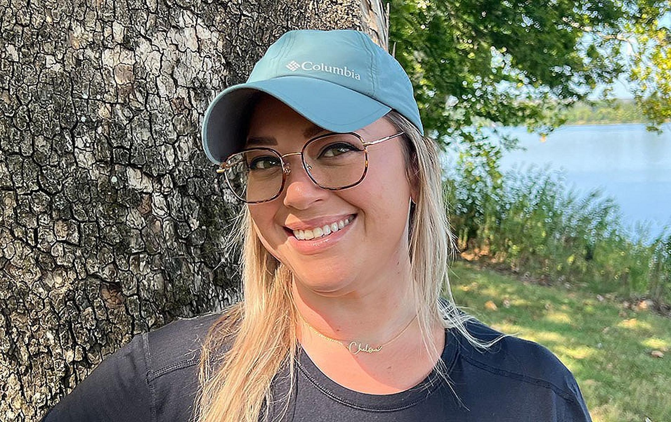 Chelsea McCurdy smiles widely for the camera at Yellowstone National Park wearing a Columbia Sportwear Coolhead II ball cap with a beautiful lake behind her.