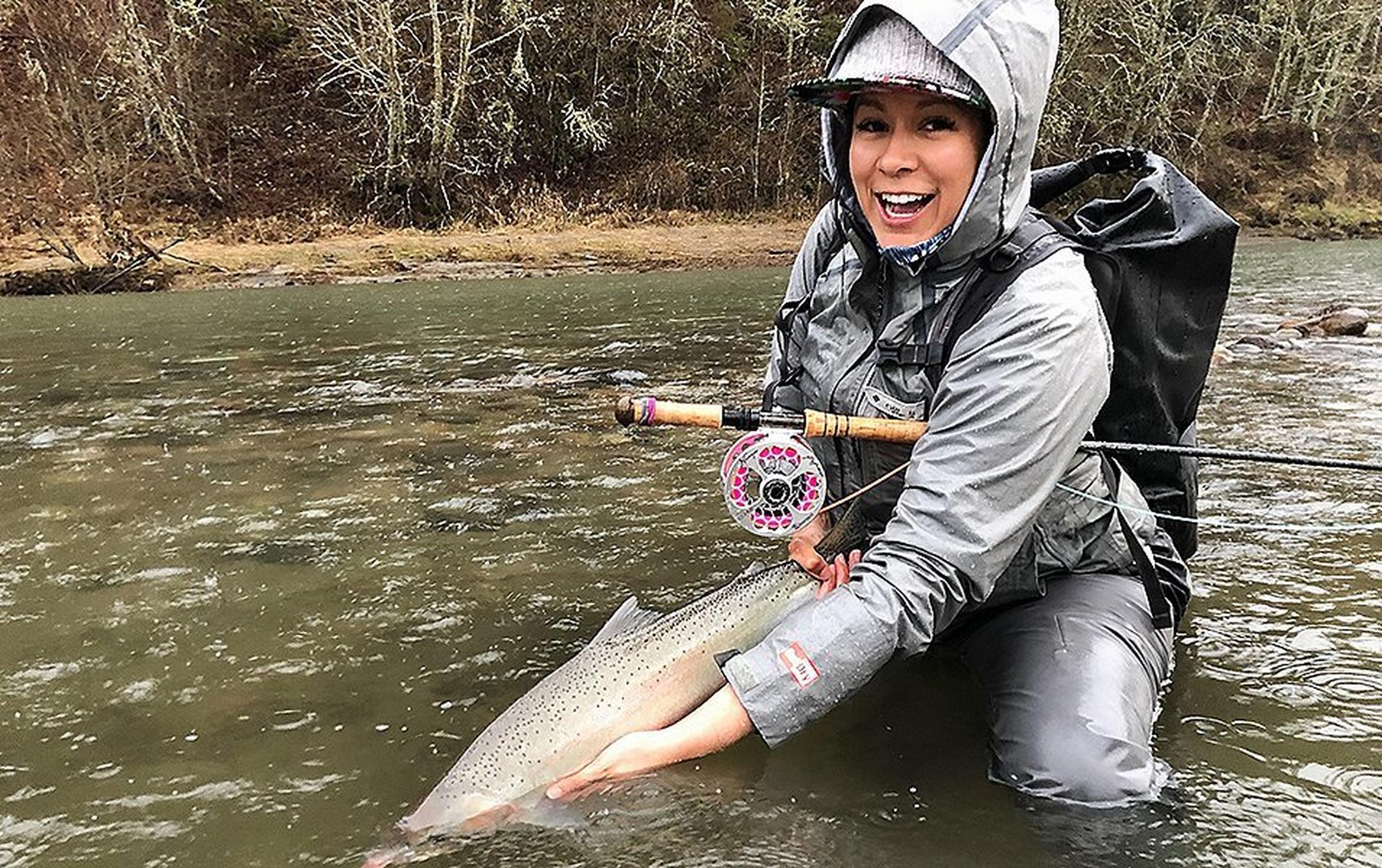 Ruth Sims holding a fishing in a running river.