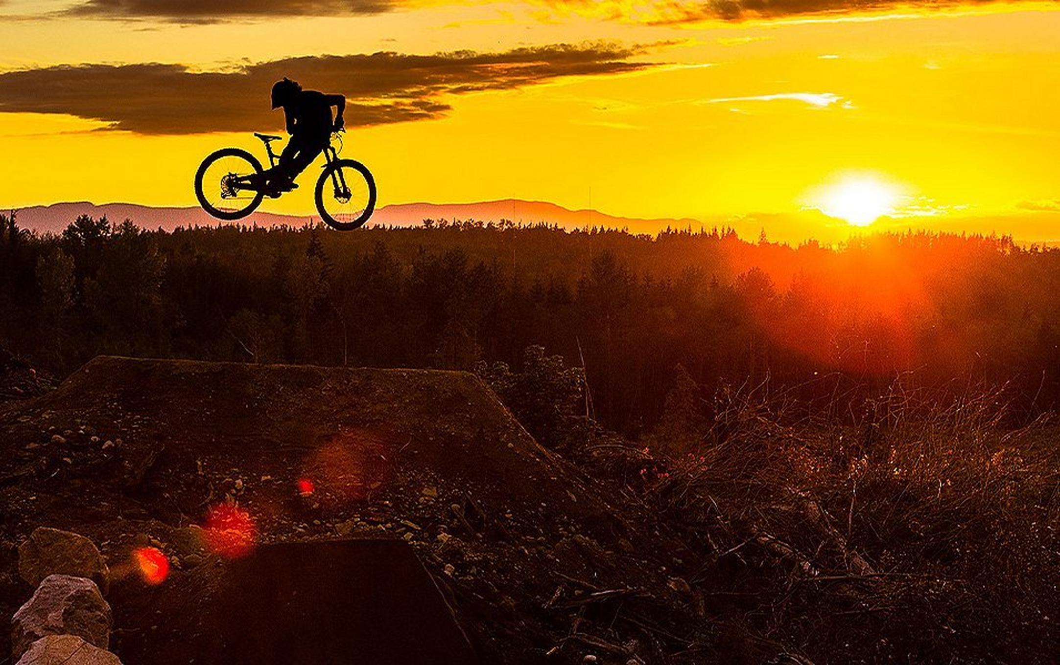 Biker jumping off a ramp at sunset.