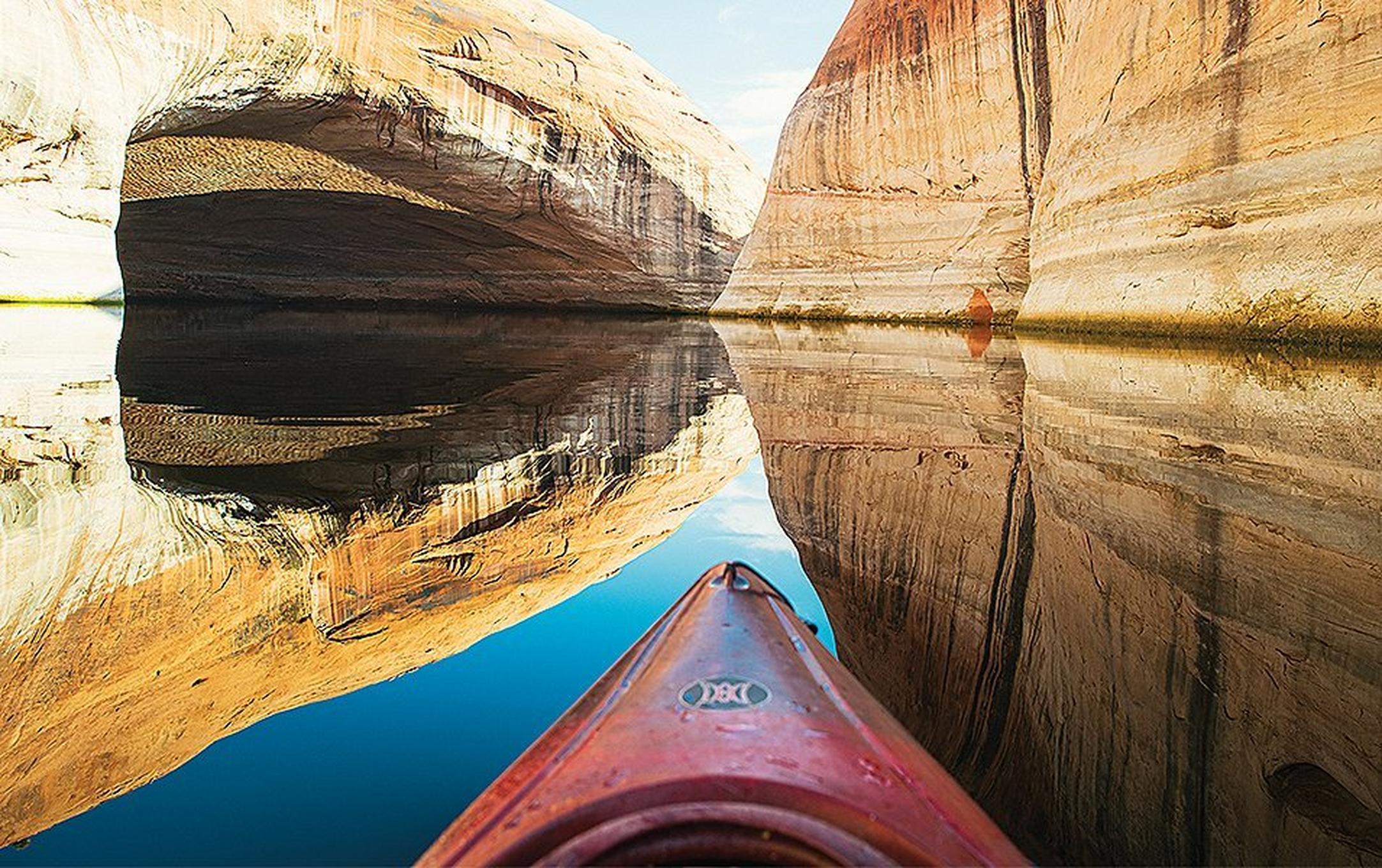 A point-of-view shot showing the tip of a kayak in front of a beautiful river canyon.