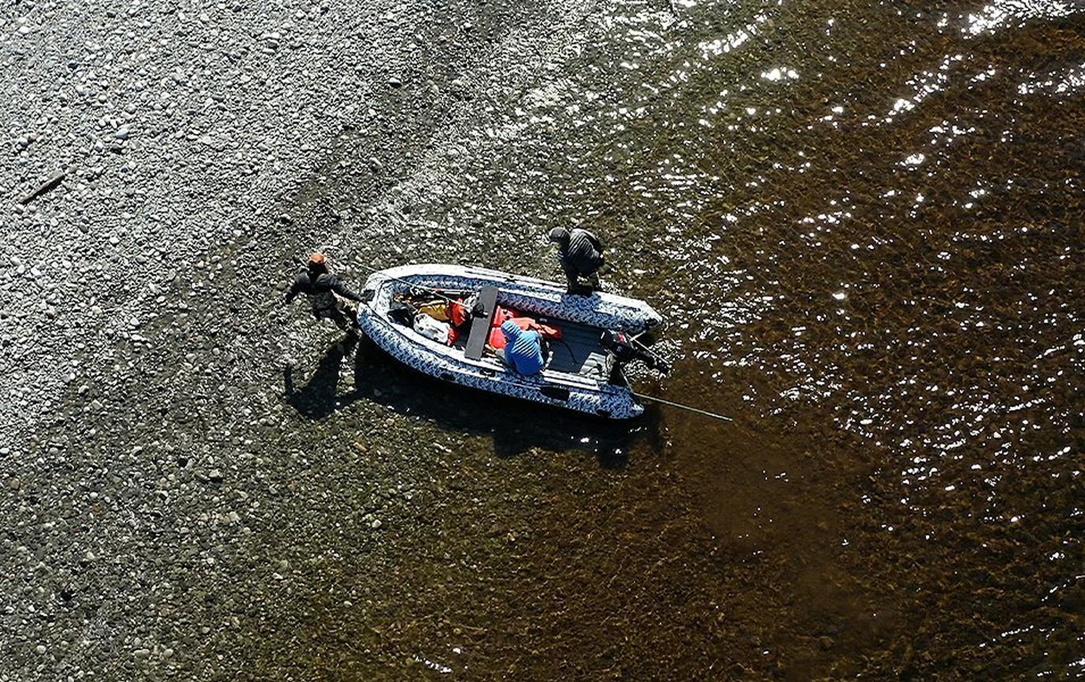 Two men pull a raft into the river while a third sits in the boat.