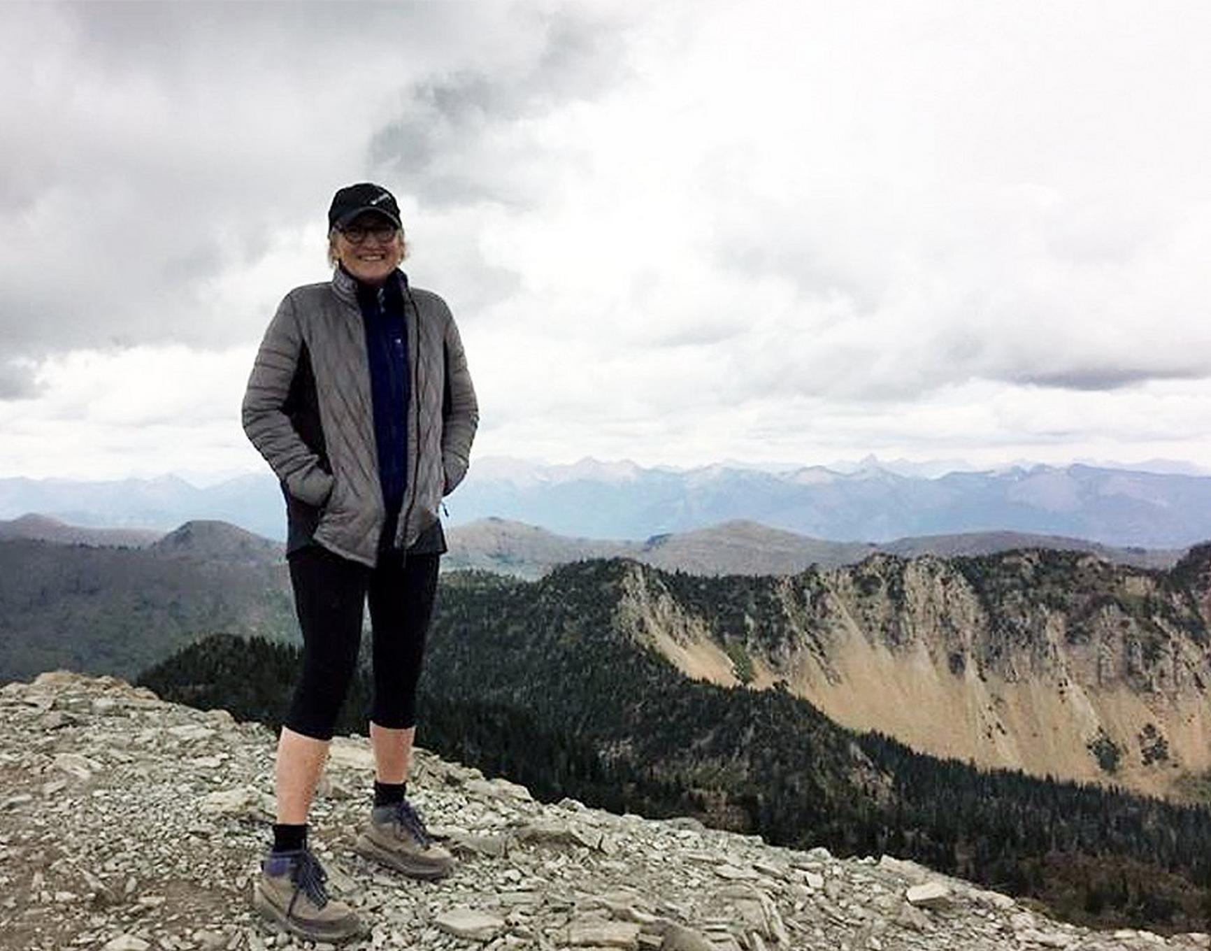 Linda Black Regnier stands on Mt. Aeneas Summit Trail in Montana looking at the camera.