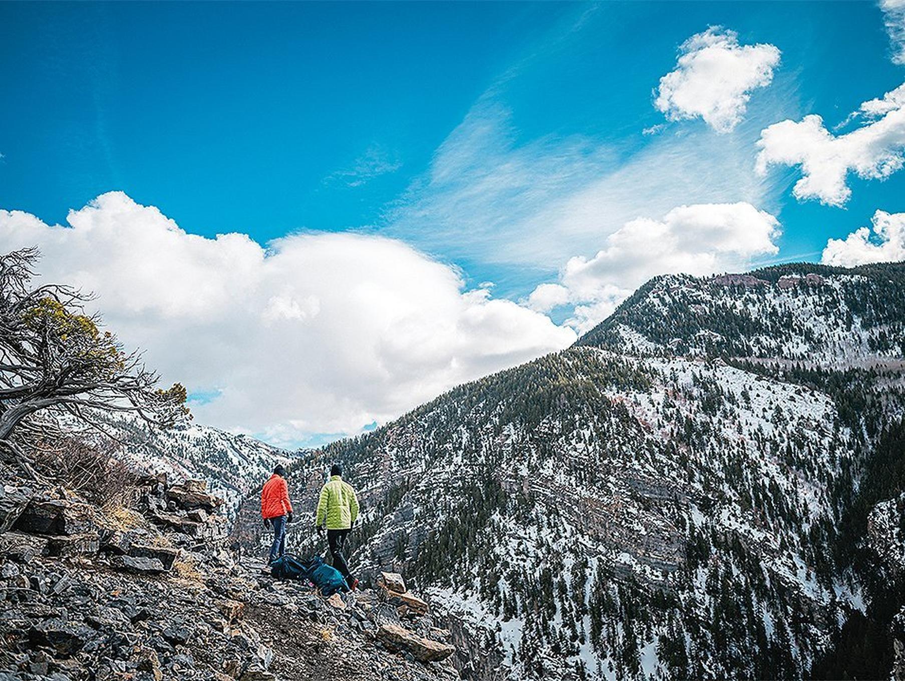 A pair of hikers walk through the mountains on a scenic trail.