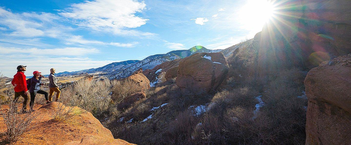 A trio of hikers stands on top of a gorgeous cliff looking out at the scenery.