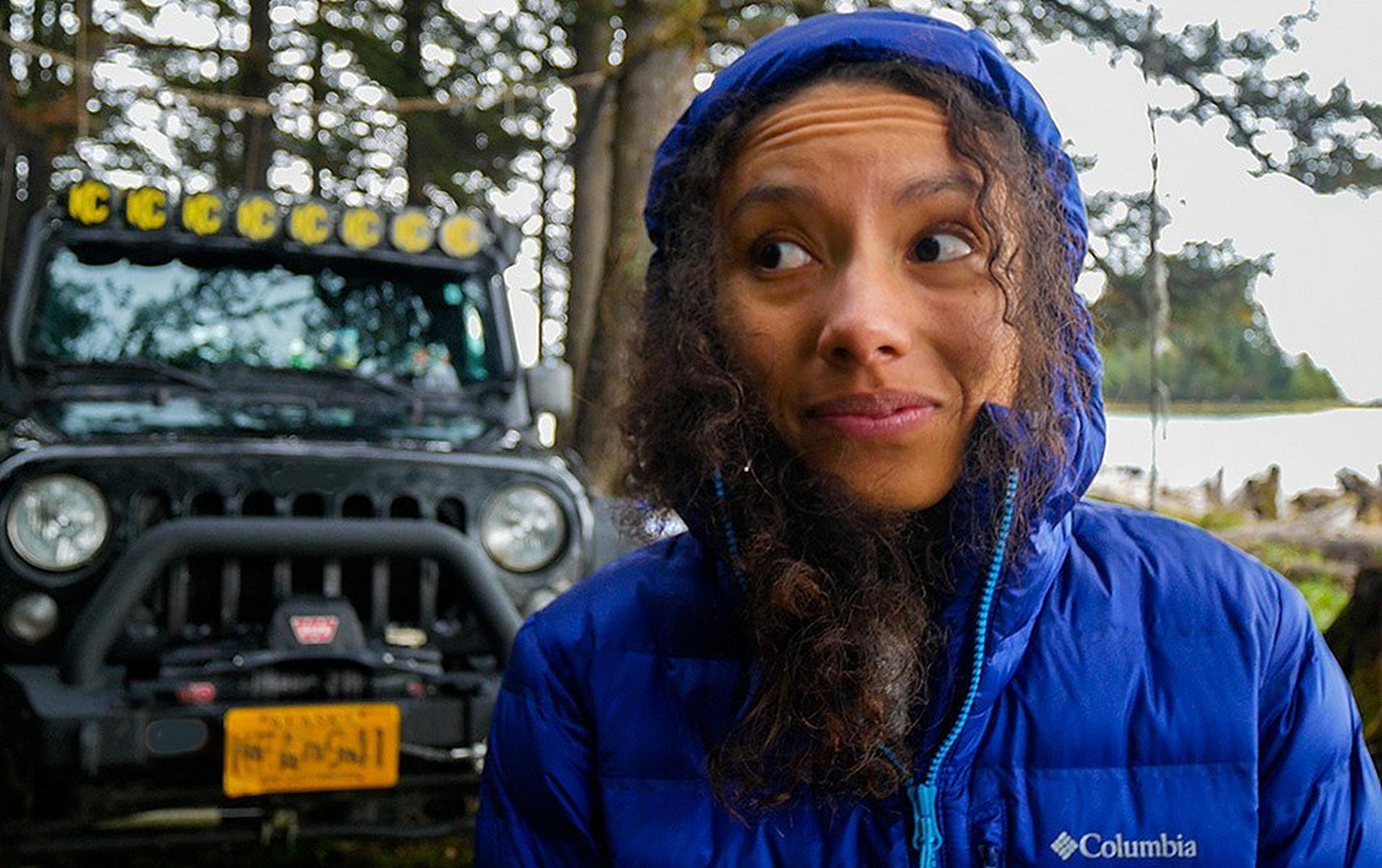 A woman stands in front of a Jeep on an overlanding excursion wearing a blue Columbia Sportswear jacket.