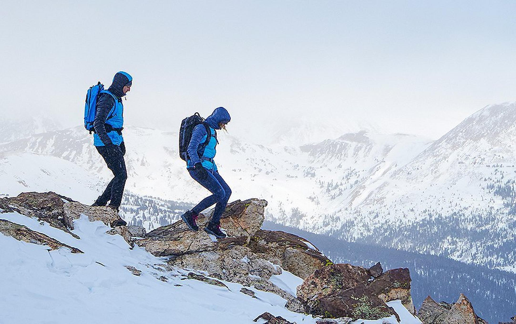A pair of hikers walks down a snowy mountain on a cold winter day wearing Omni-Heat Infinity jackets.