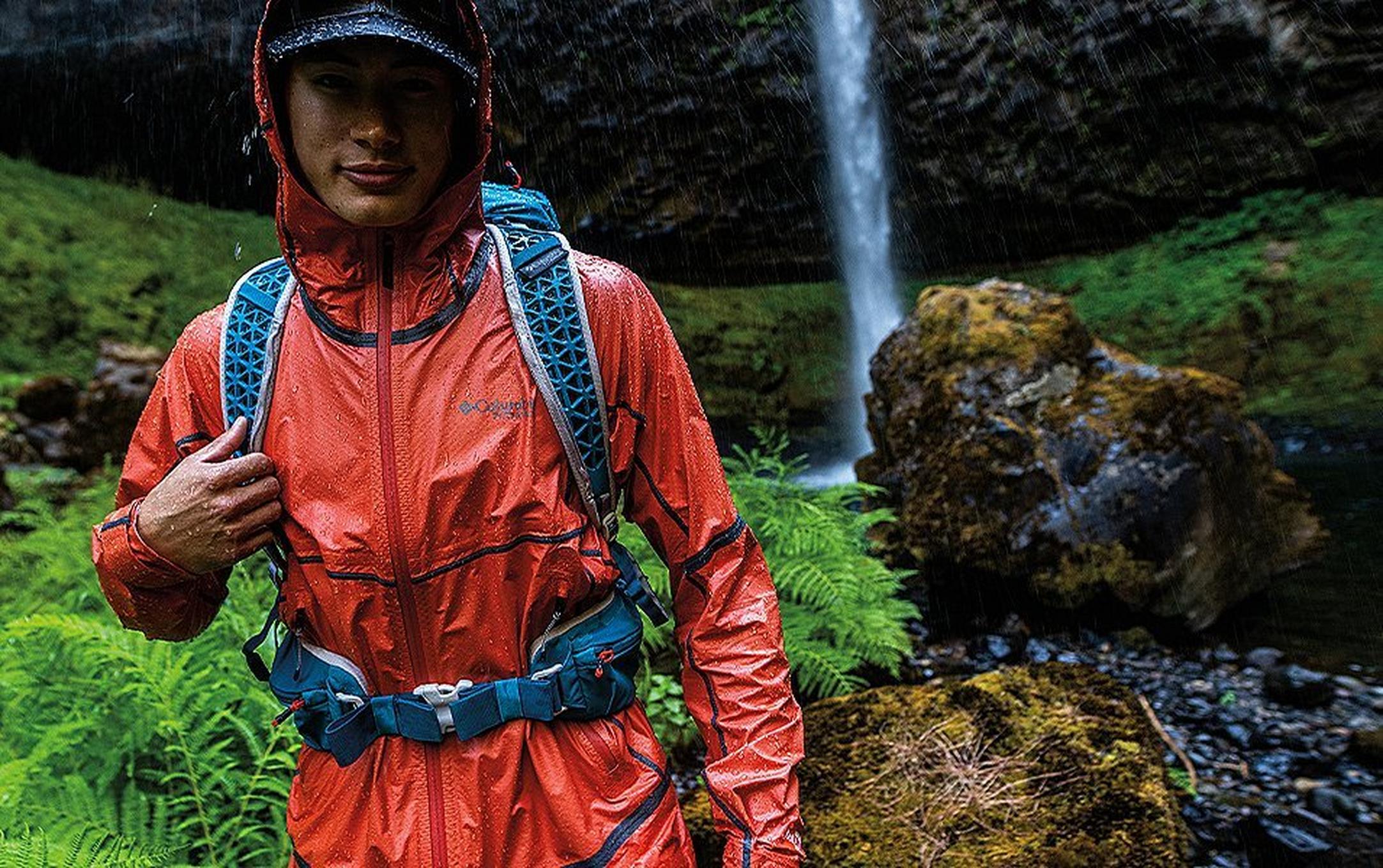 A man hikes through a wet scenic rainforest wearing a waterproof jacket.