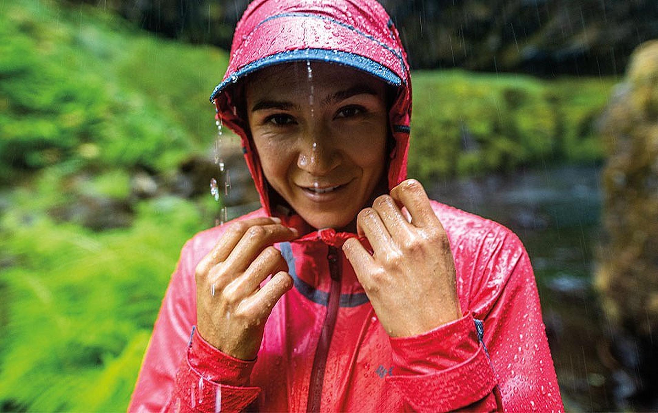 A closeup of a woman wearing rain gear smiling in the rain.