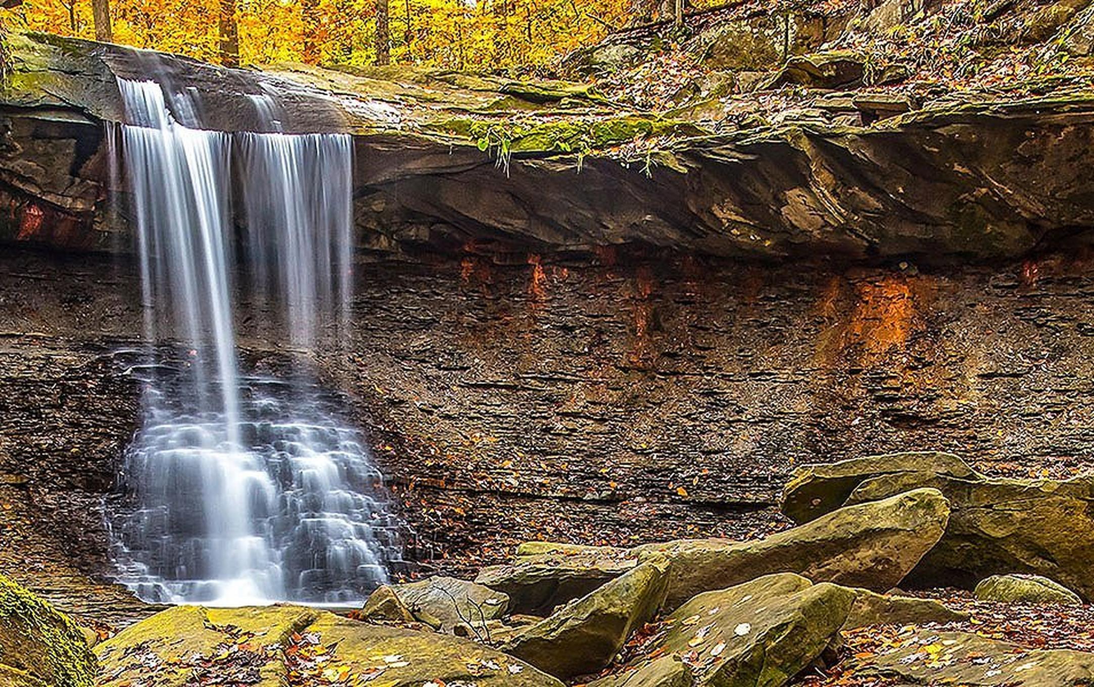 A scenic waterfall plunges over a bed of rocks amid orange and yellow trees at Ohio’s Cuyahoga Valley National Park.