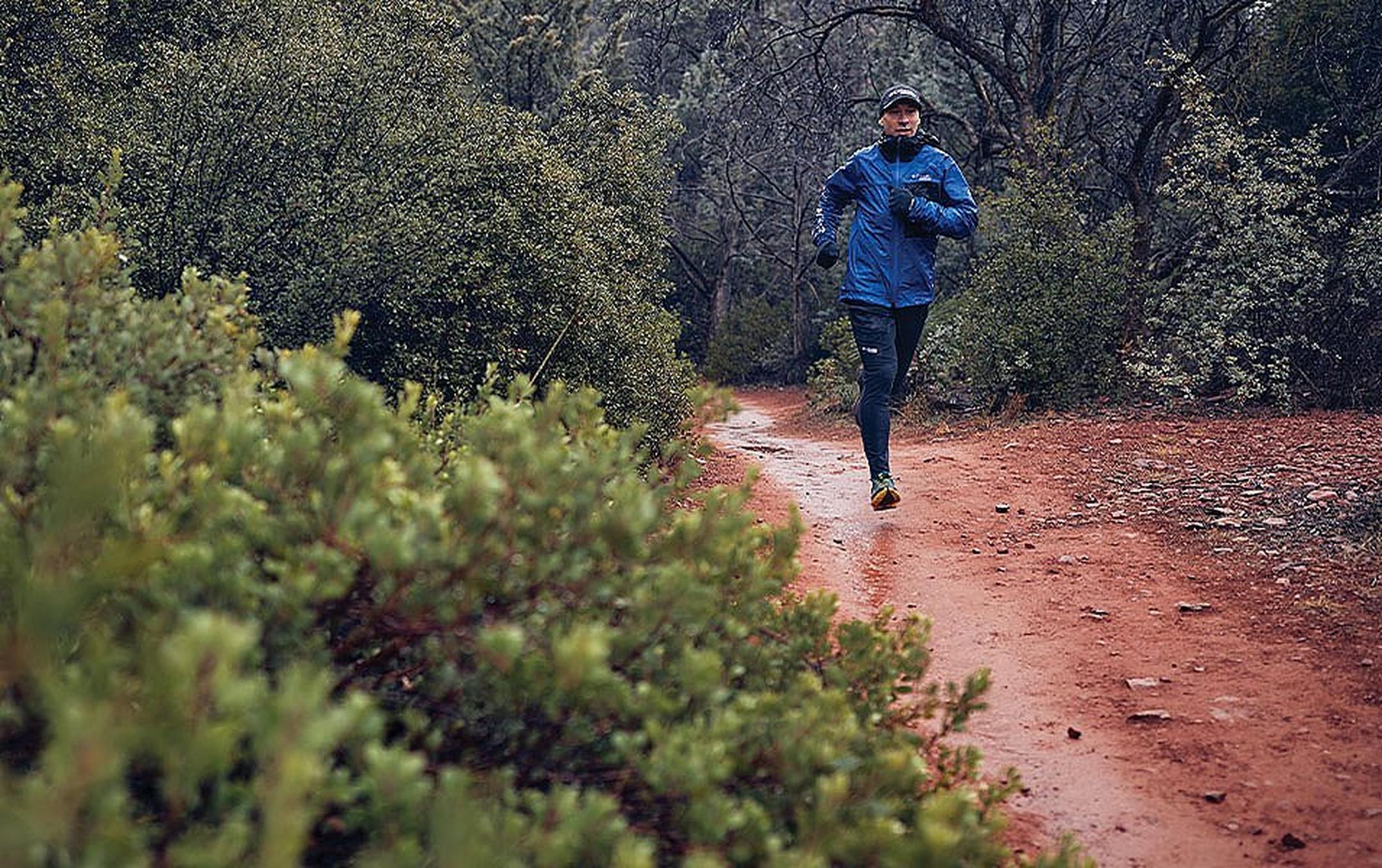 Man running down a muddy trail in the rain.