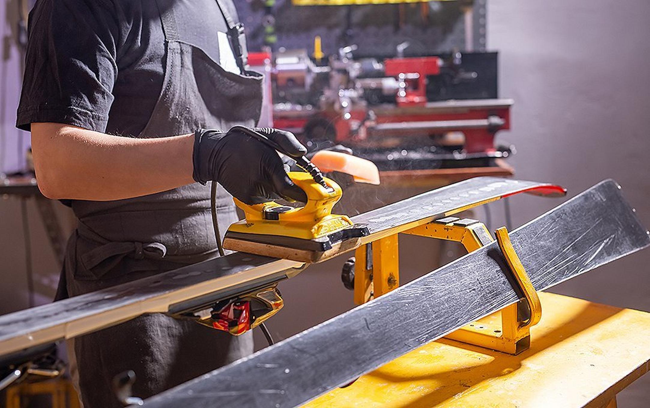 A man irons wax onto a set of skis in a garage-style workshop.