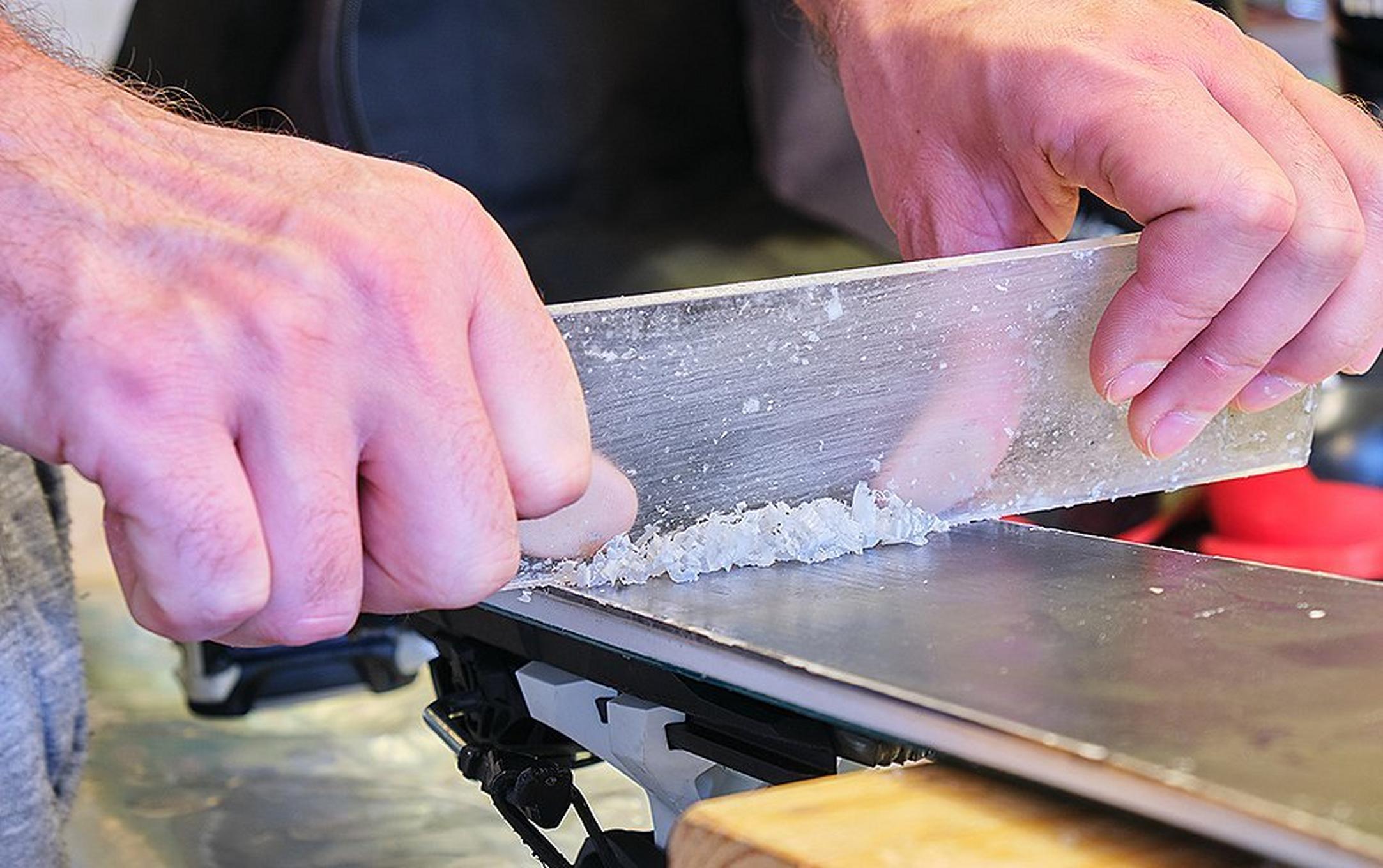 A close-up shot of a skier’s hands scraping wax off a set of skis.