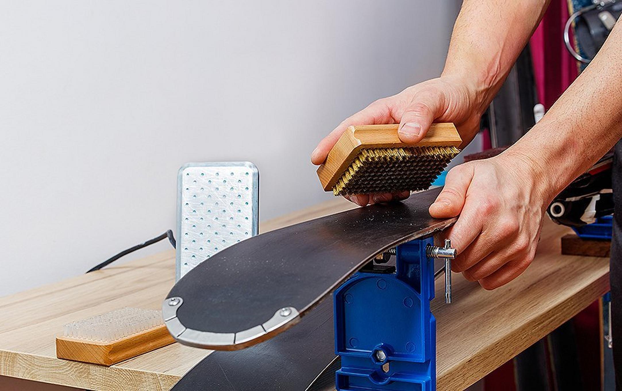 A pair of hands are pictured brushing wax off of a set of skis.