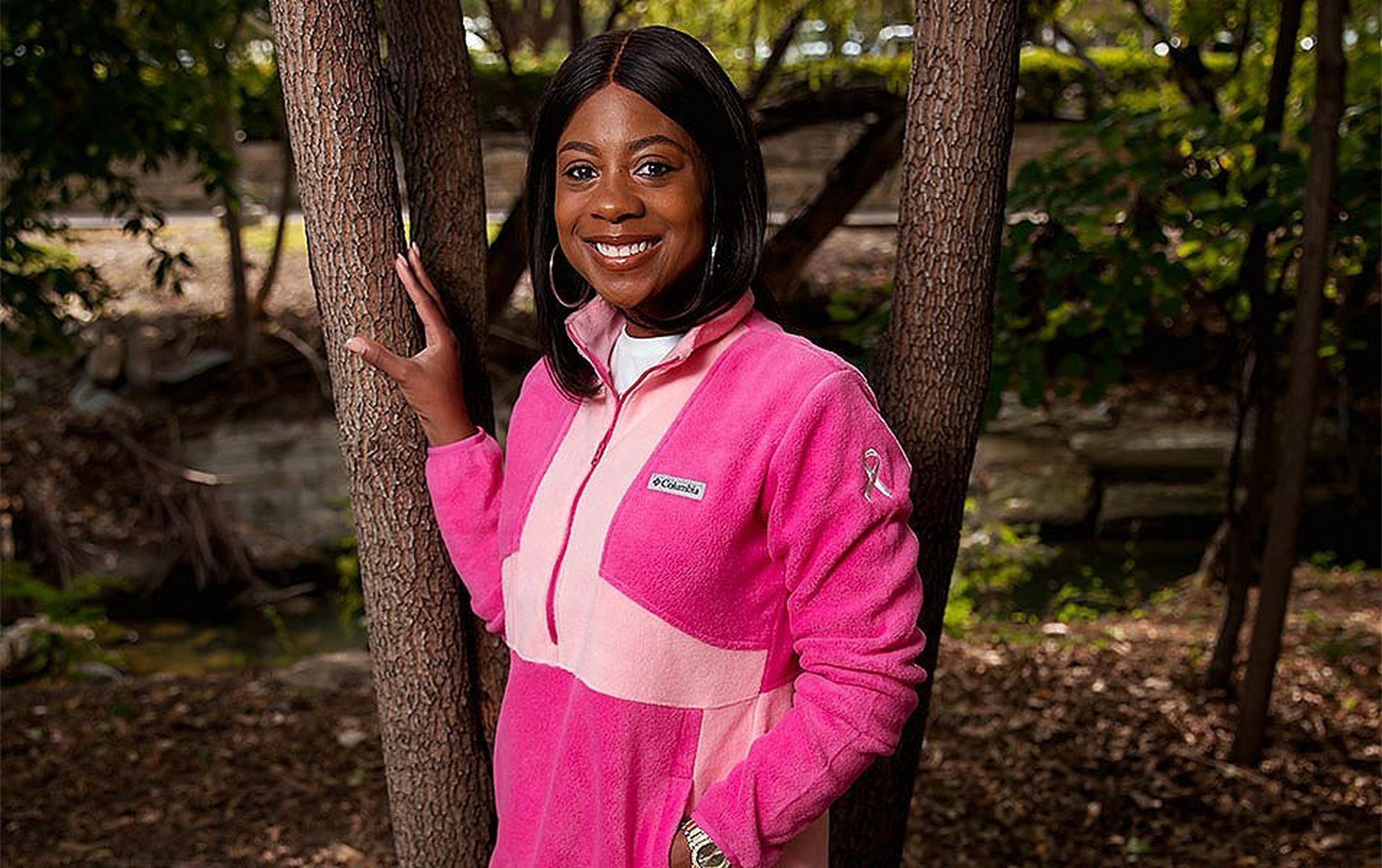 Catrin a Crutcher stands in front of a tree outside wearing a pink Columbia Sportswear fleece with a National Breast Cancer Foundation logo