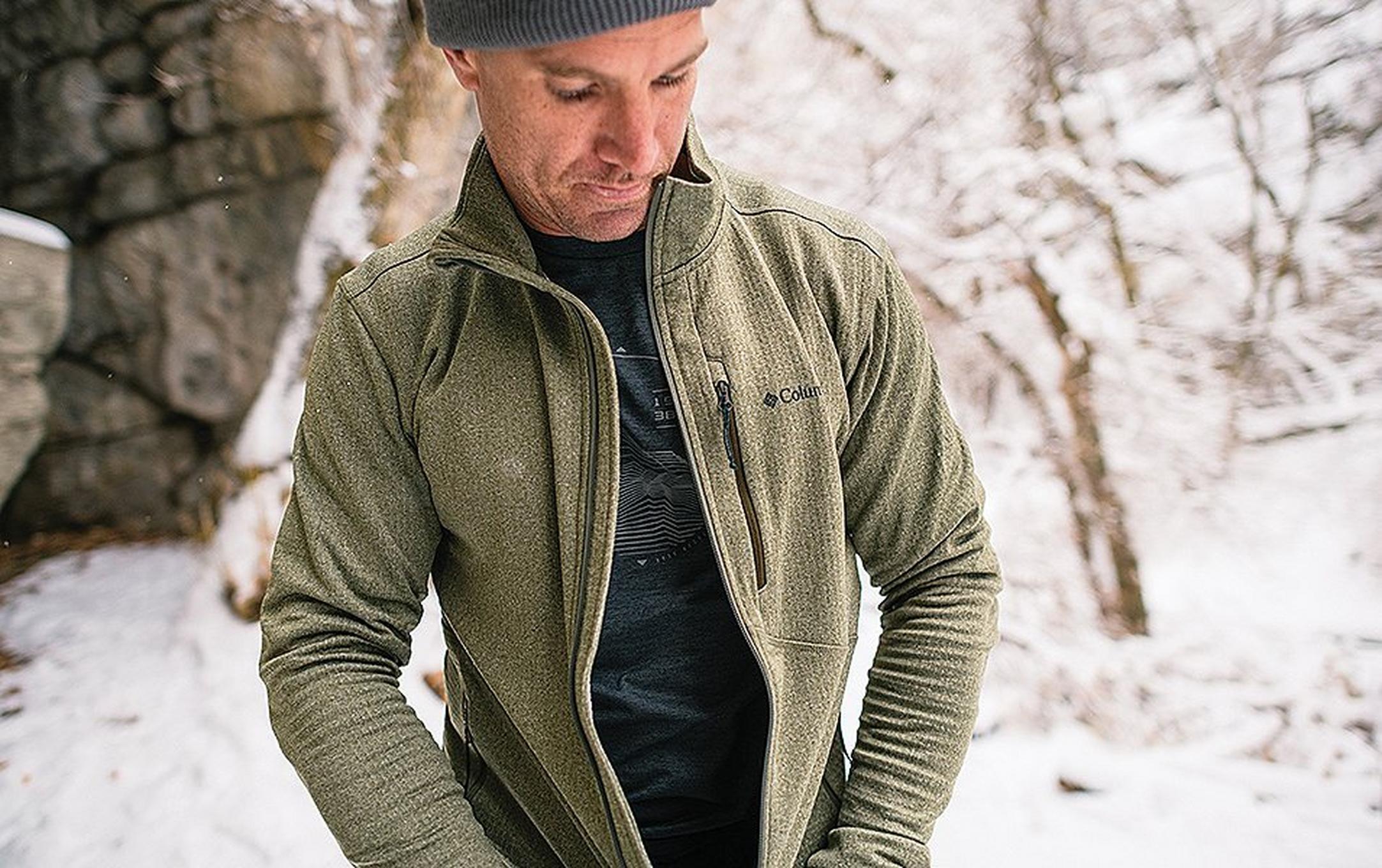 Man zipping up coat in a snowy landscape.
