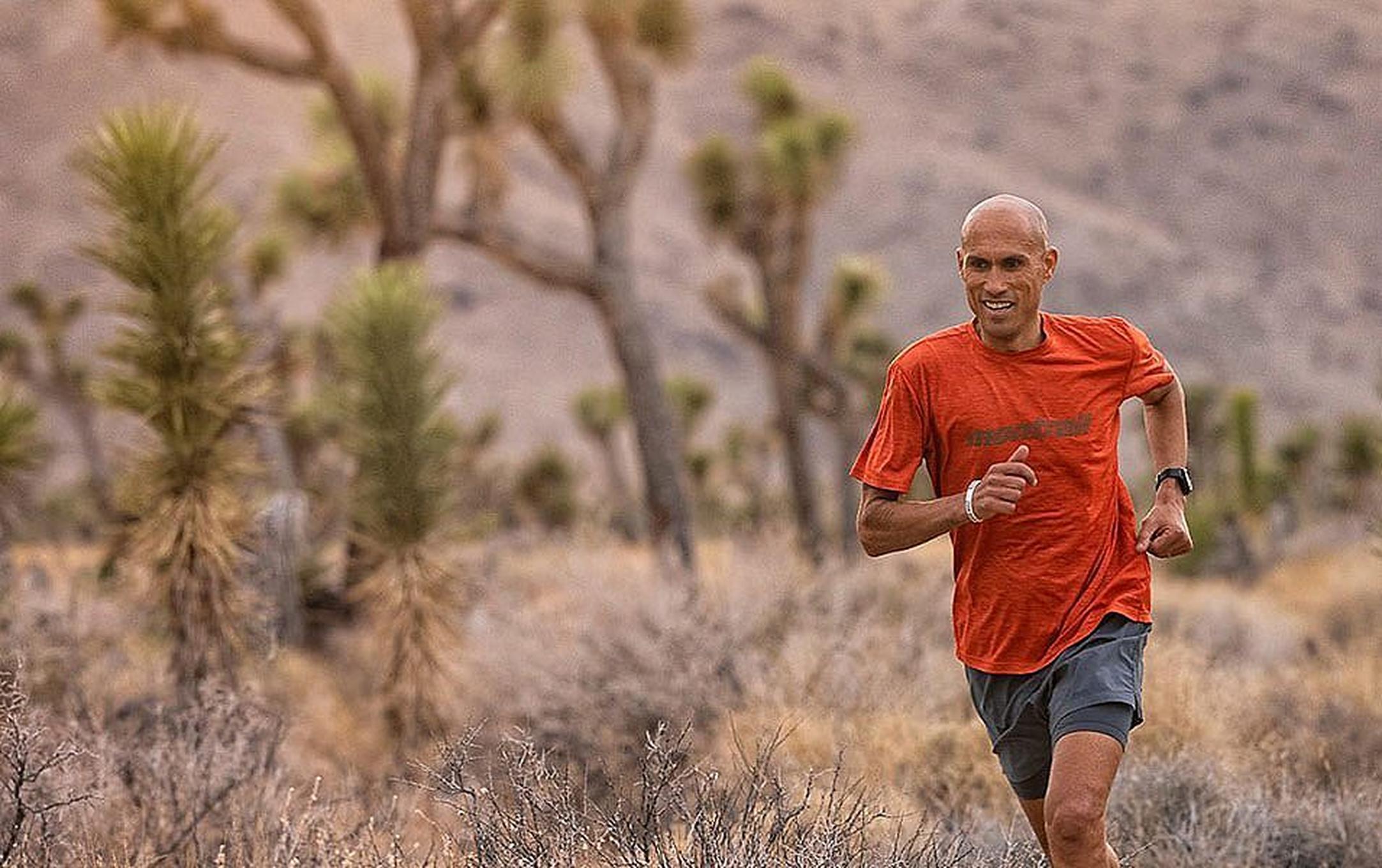 Professional athlete Yassine Diboun runs through the high desert with a smile on his face wearing a red Montrail shirt.