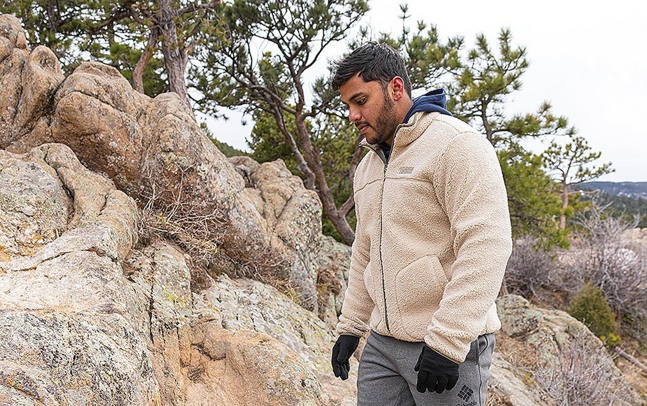 A man walks on a rocky trail wearing a white fleece jacket and black gloves.