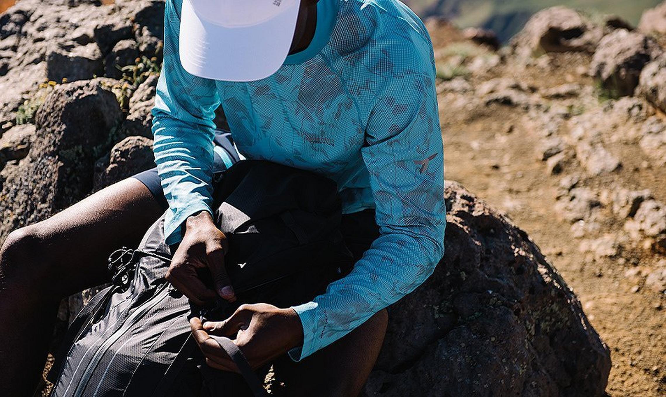 A man sitting on the ground packing up his backpack.