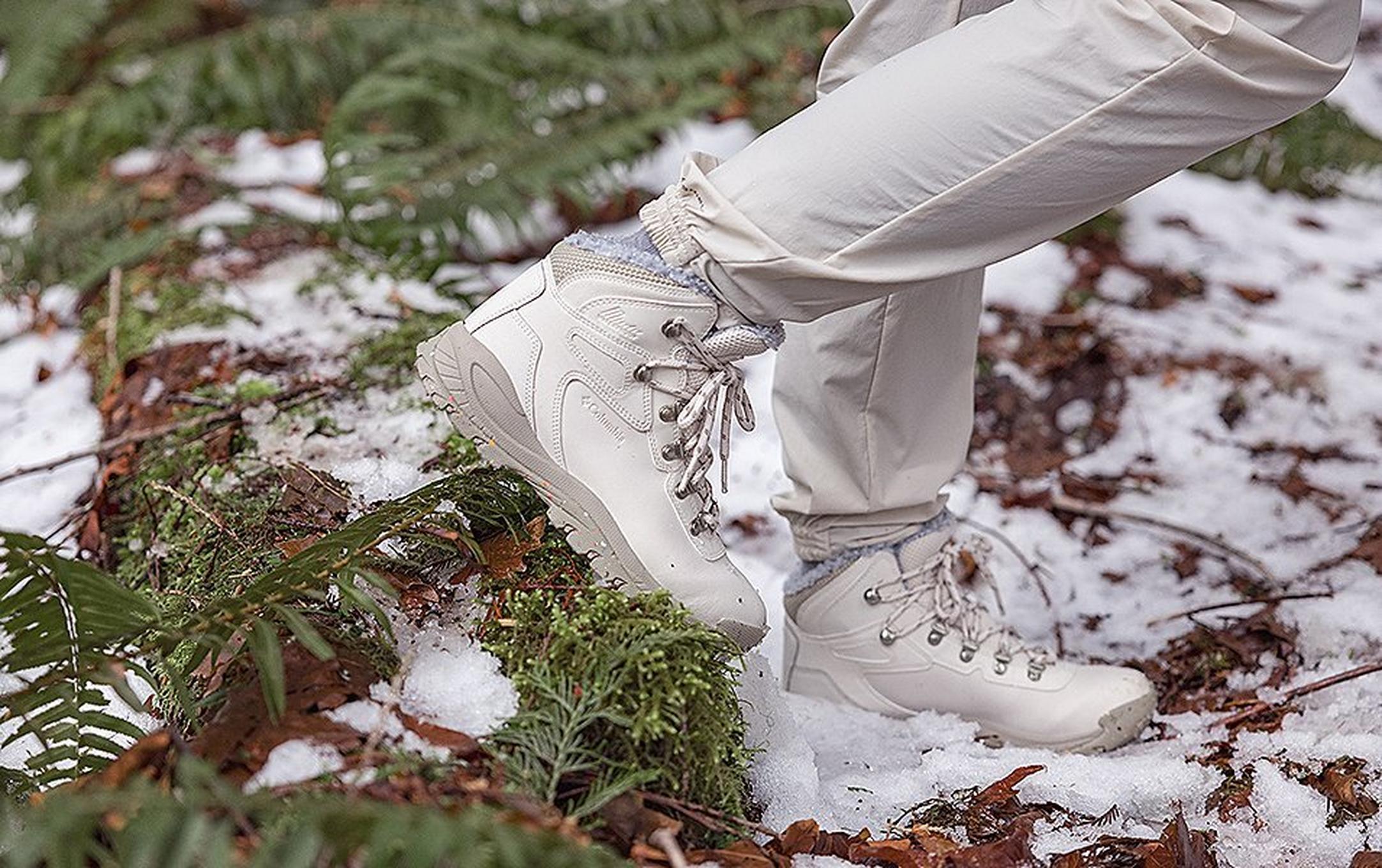 A close-up shot of a pair of white Columbia Sportswear boots walking in a snowy setting.