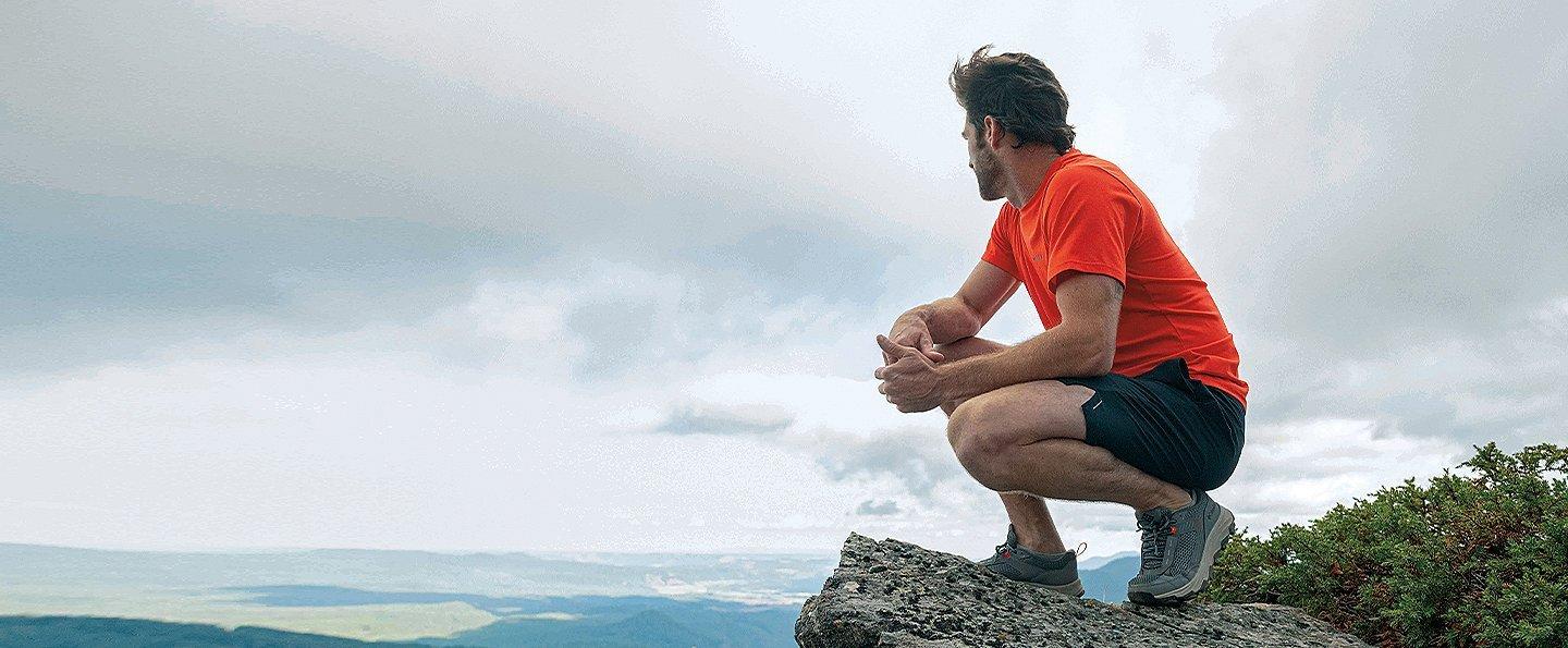 Man perched on rock outcropping looking out.