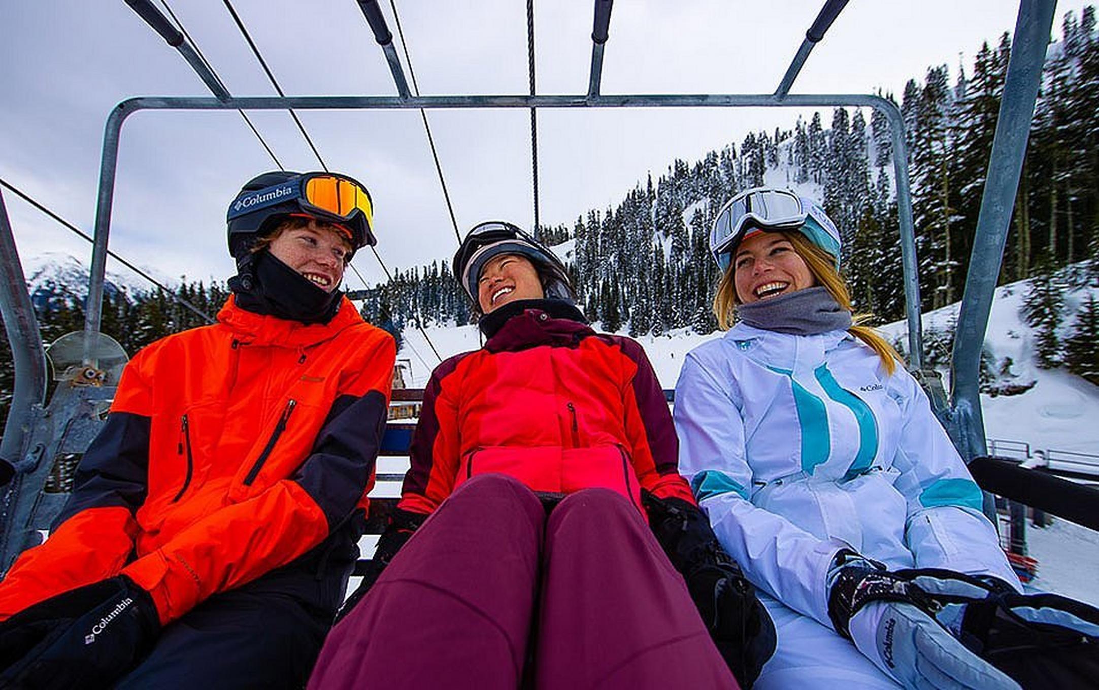 Three skiers ride a chairlift laughing and enjoying themselves on a beautiful winter day.