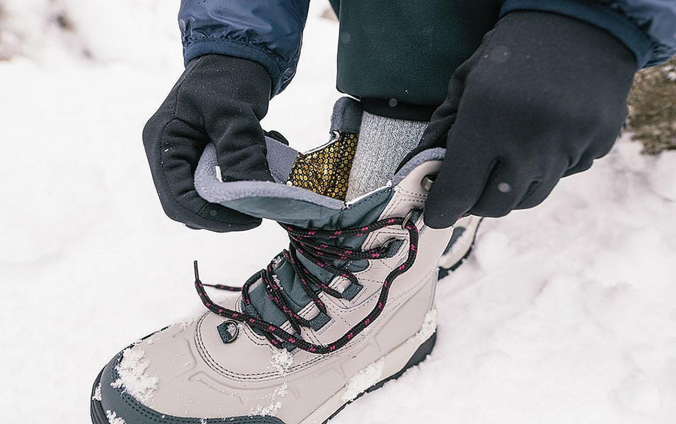 A close-up shot of a man crouching down and tying a white Columbia Sportswear winter boot in the snow