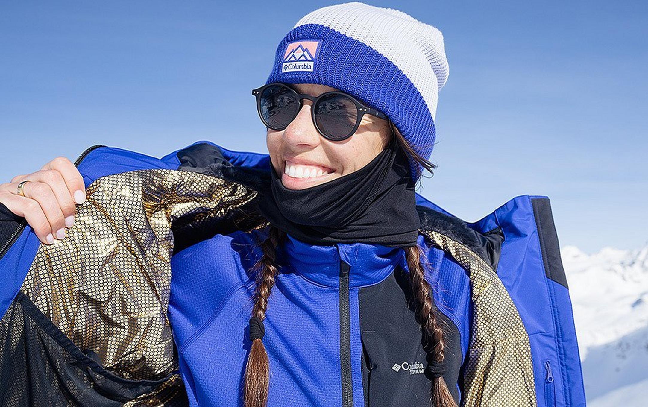 A female skier smiles as she dons a warm winter jacket.