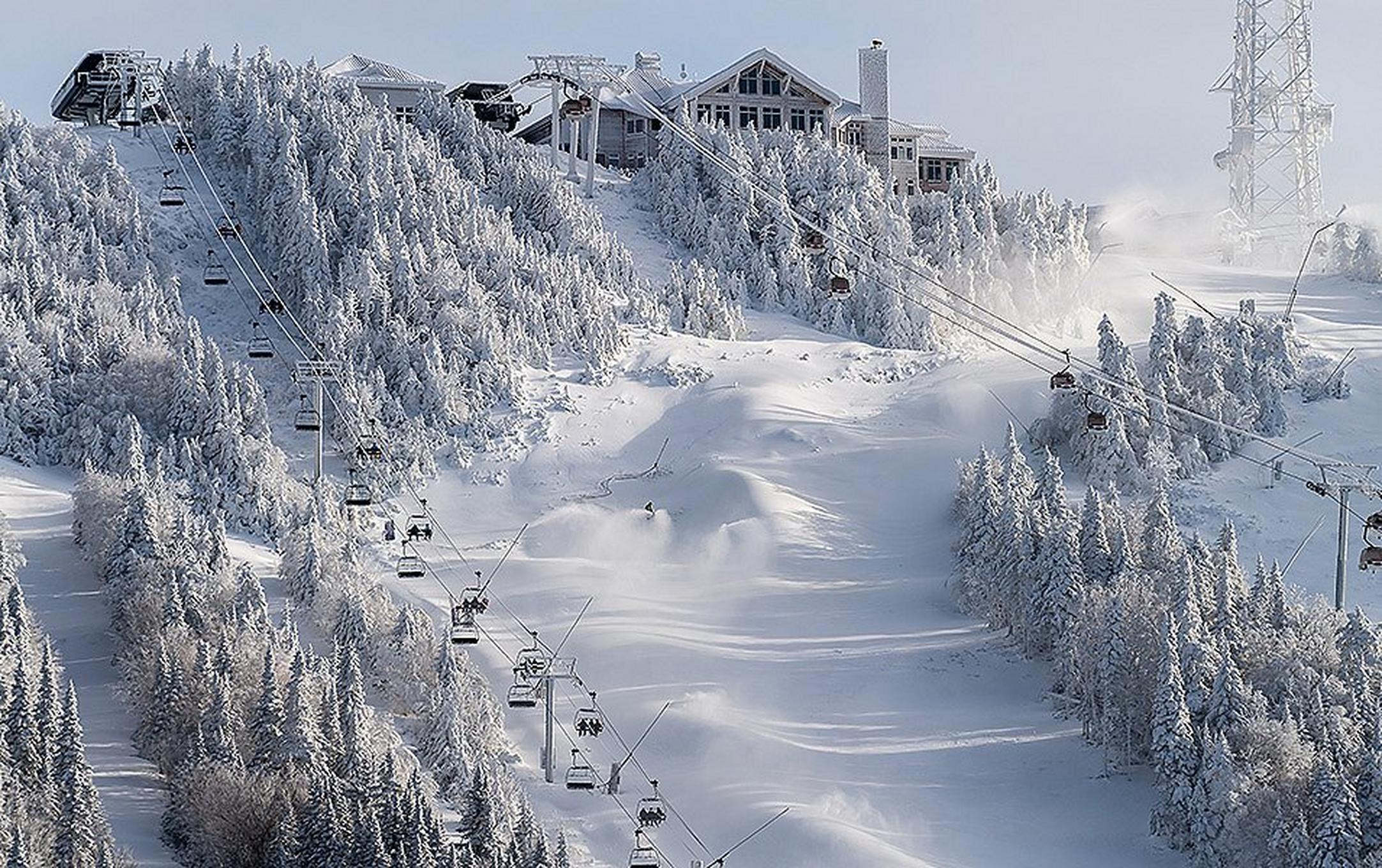 Two chair lifts snake up a snow-covered mountain. At the top is a ski lodge.