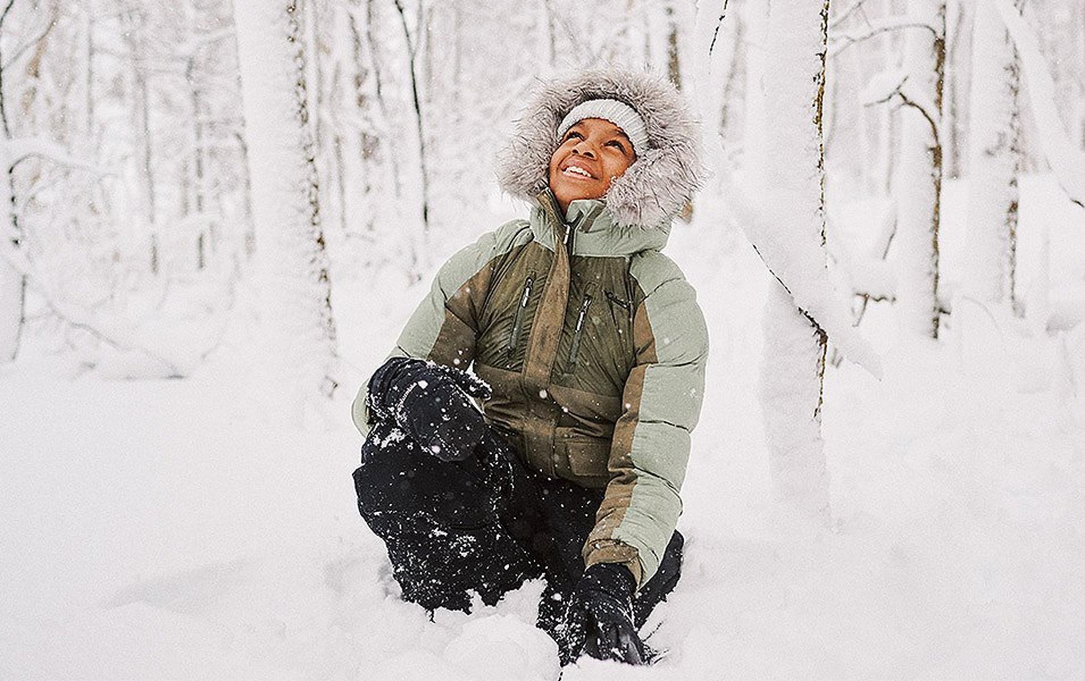 A person with big puffy jacket and faux fur lined hood enjoys playing in the deep snow.