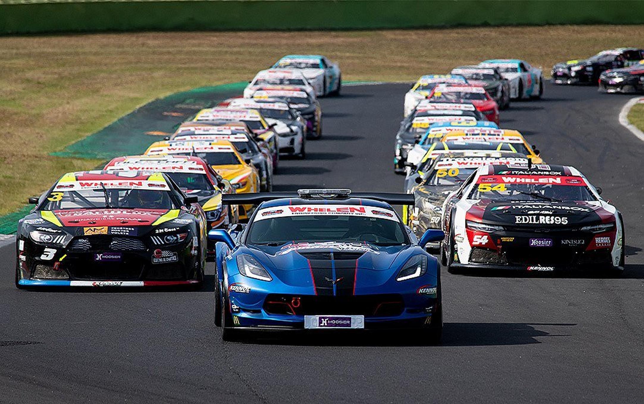 NASCAR race cars form two lines on the track behind a lead car.