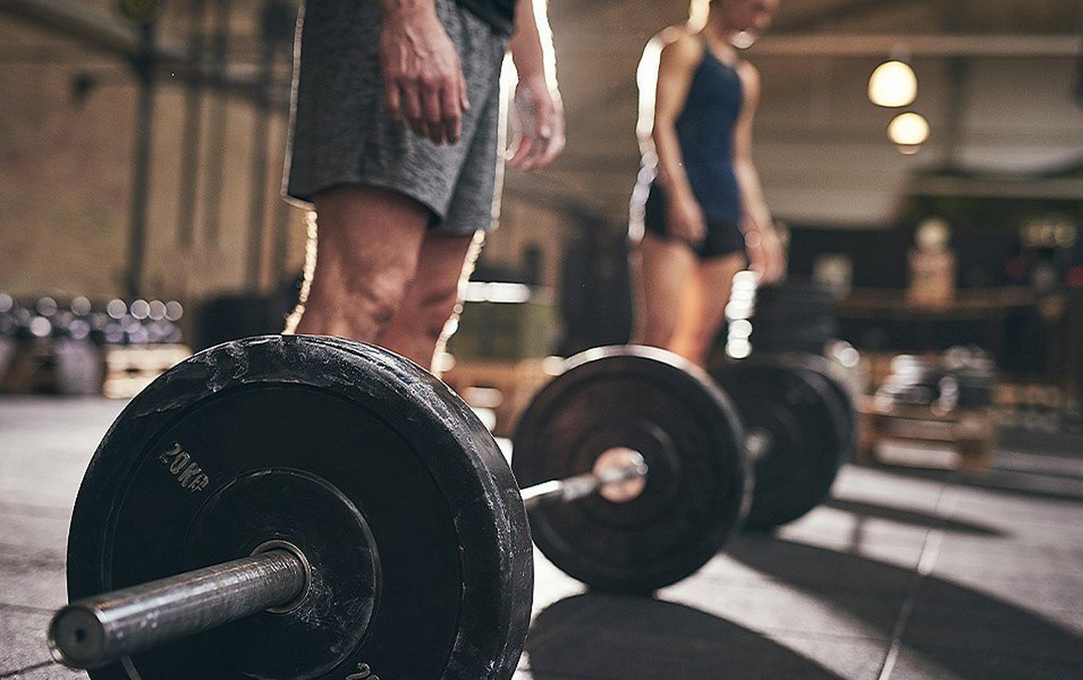 Two people prepare to perform squats with heavy barbells in a gym.