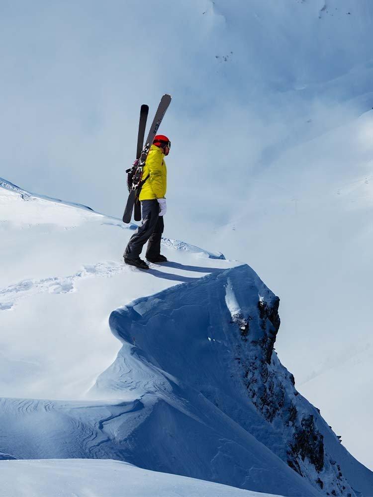 Person on the edge of a snowey cliff with skis on their back.