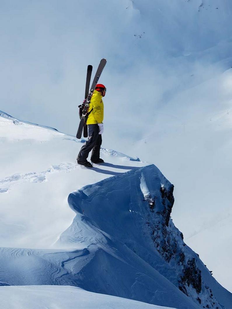 Person on the edge of a snowey cliff with skis on their back.