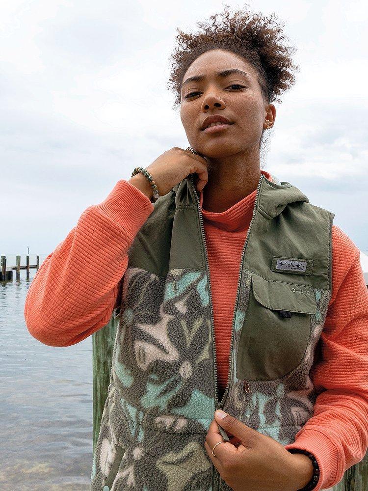 Women in and orange shirt and green vest in front of the water