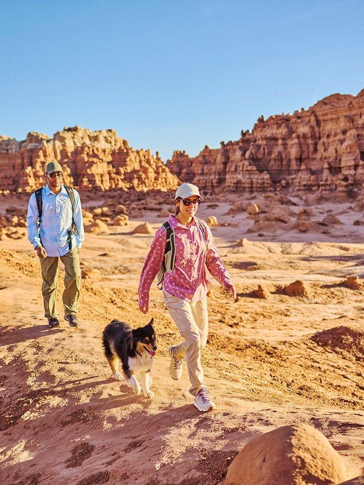 Two people and a dog hiking on a trail.