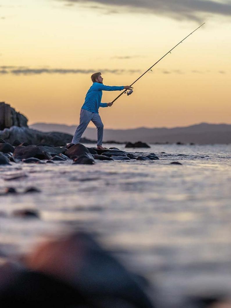 Man casting against a golden sky.