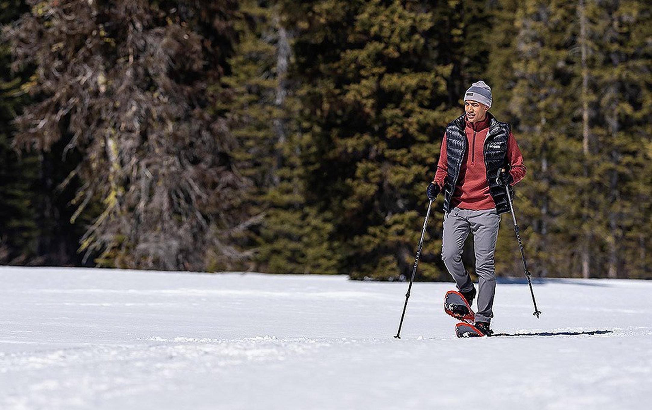 A man snowshoeing in a snowy forest clearing.
