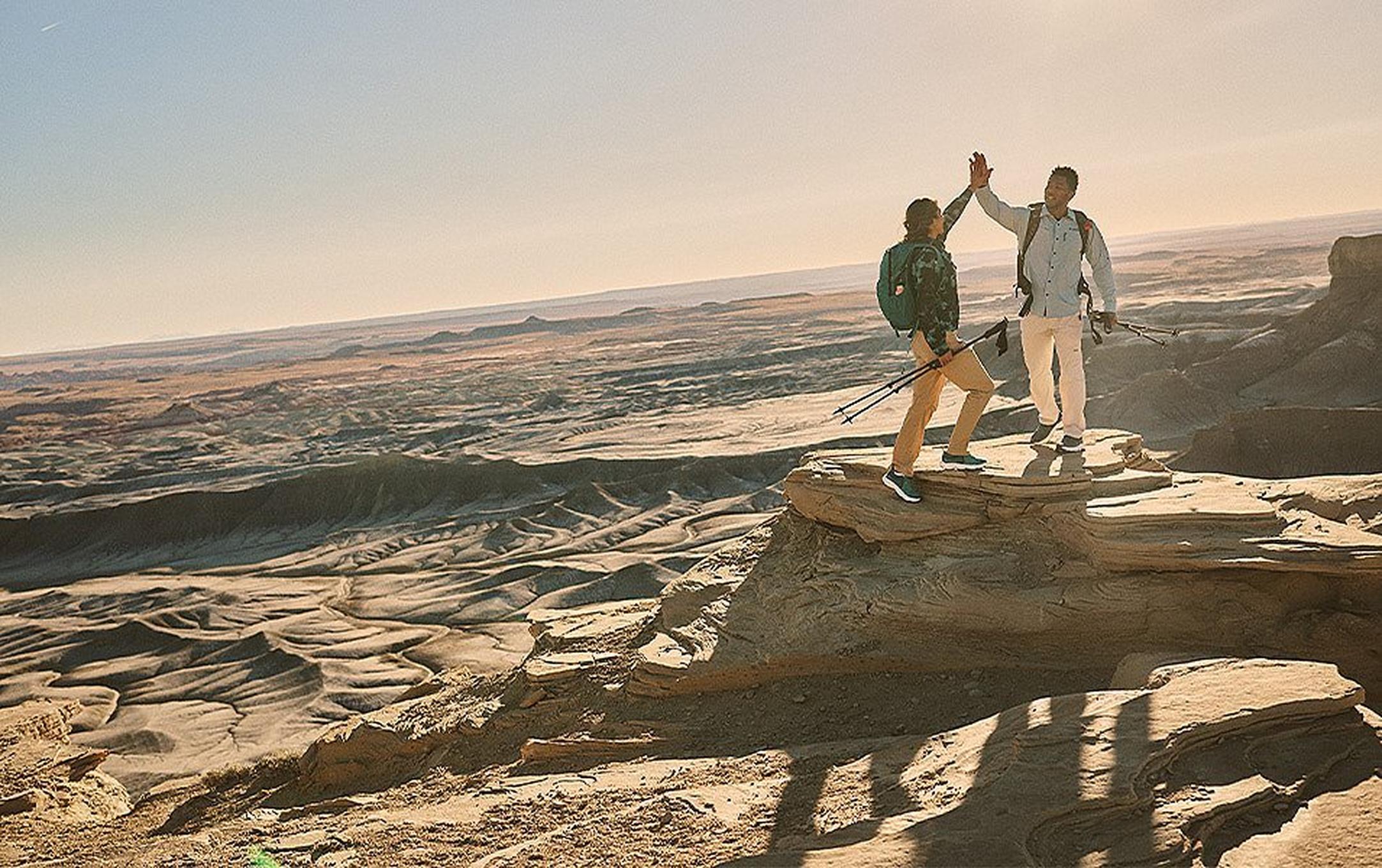 Two hikers celebrate the successful ascent of a high plateau with a high-five.