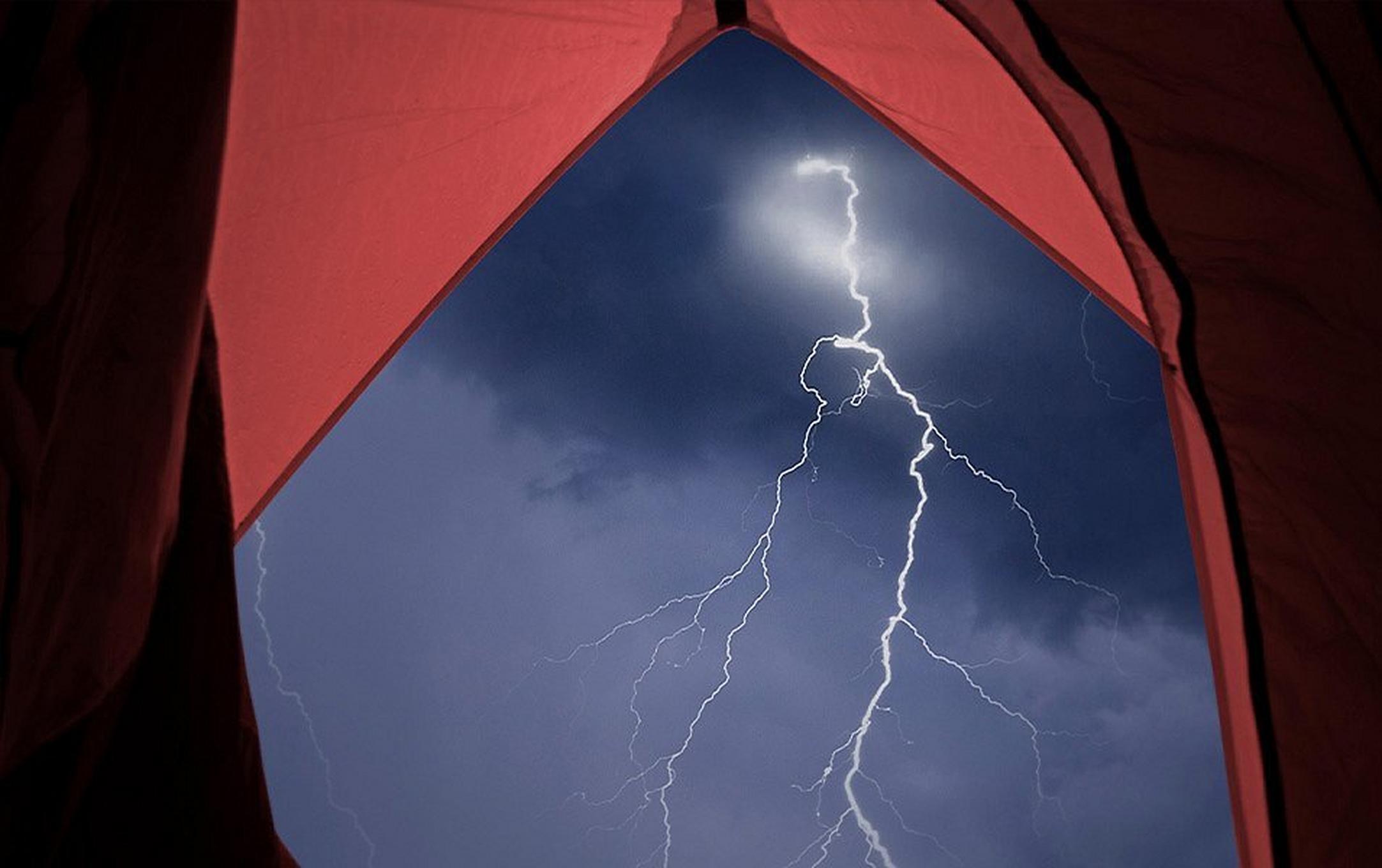 From inside a tent, you can see out of the front vestibule to the night sky. The sky is dark, and a brilliant bolt of lightning strikes the ground.